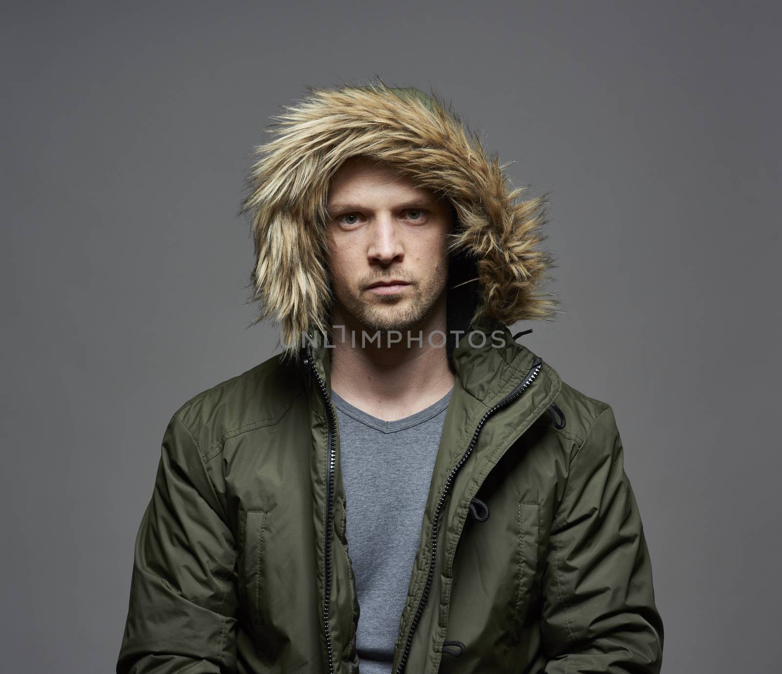 Studio portrait of young adult caucasian model wearing winter coat with hood on. Isolated on gray background.