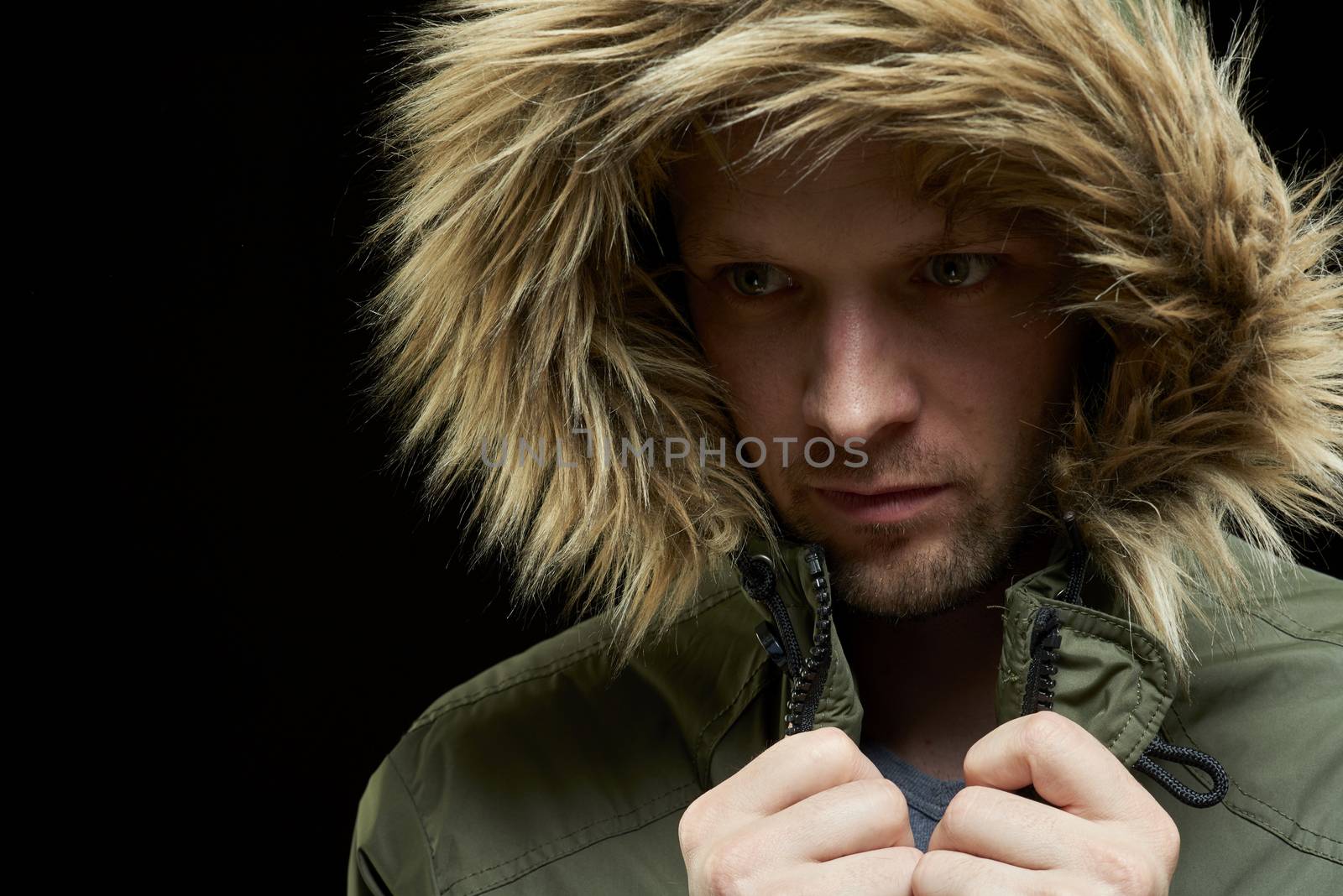Low key studio portrait of young adult caucasian model wearing winter coat with hood on.