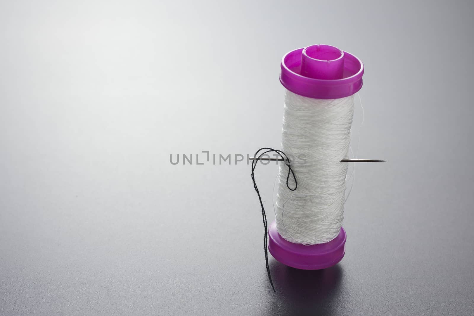 Bobbin thread with white sewing needle isolated on gray by mailos