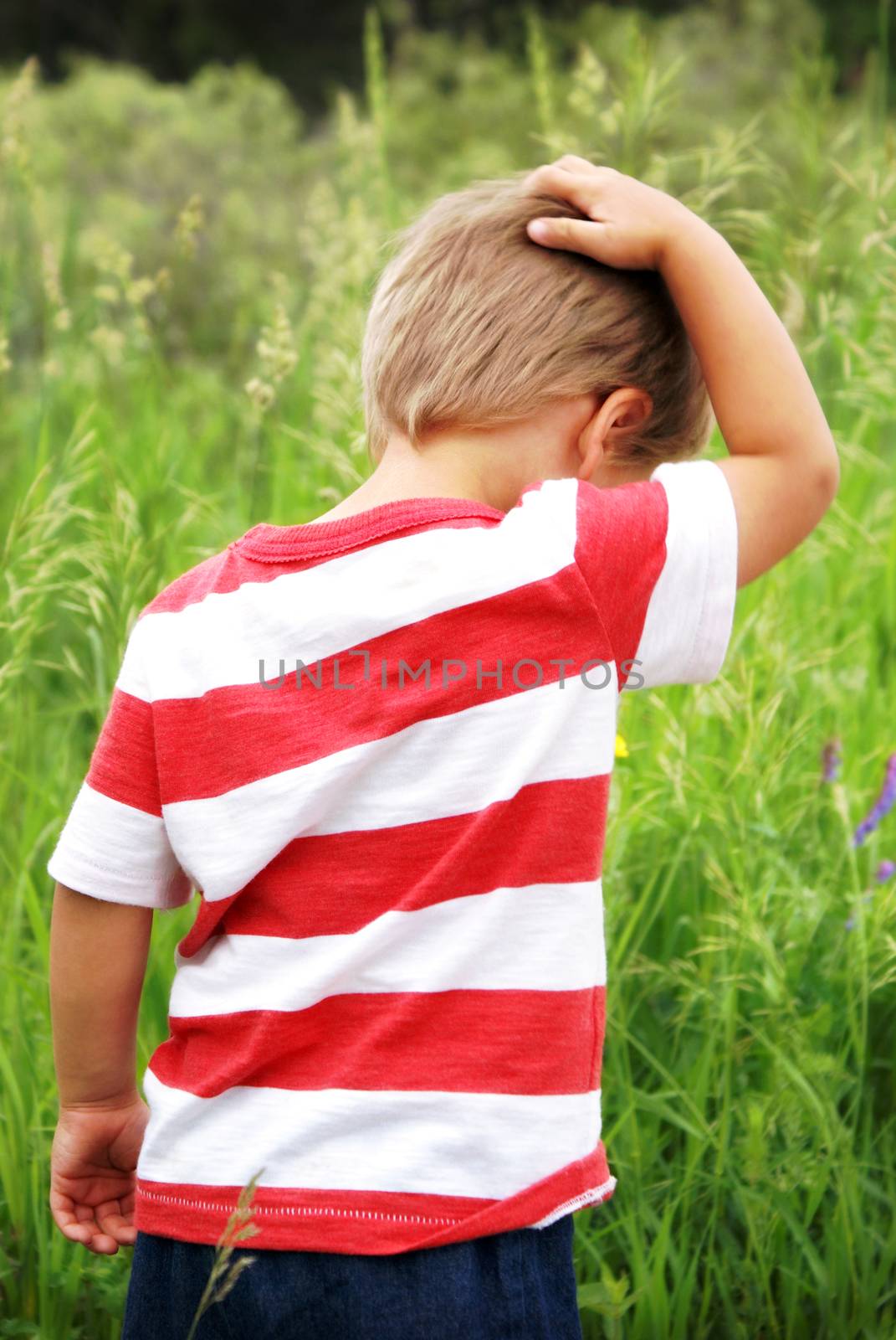 A young boy explores the great outdoors while creating some thoughts in this candid image of him scratching his head during his boyhood sense of wonder.