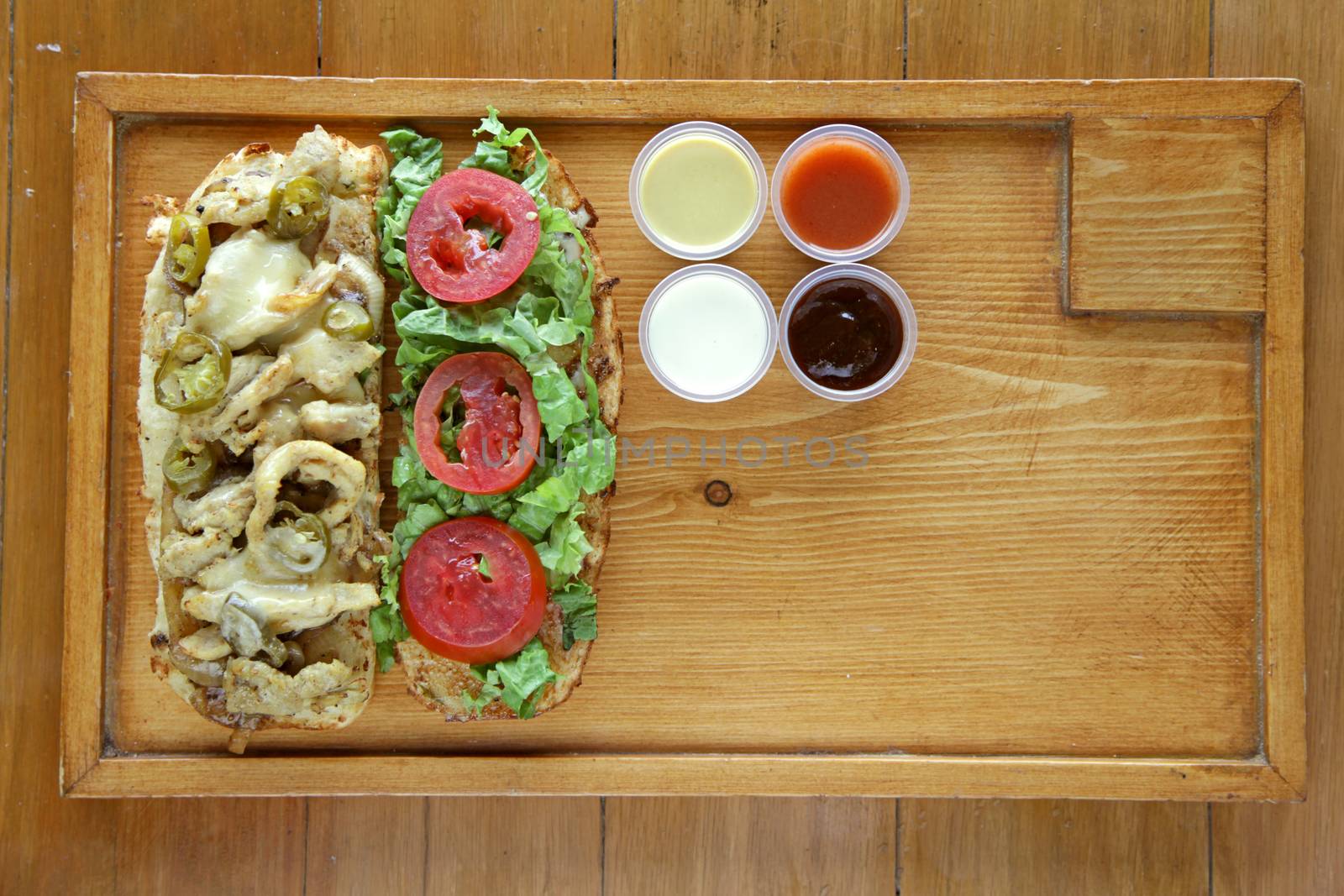 Open face healthy meat and vegetable sandwich served with condiment sauces on a wooden tray 