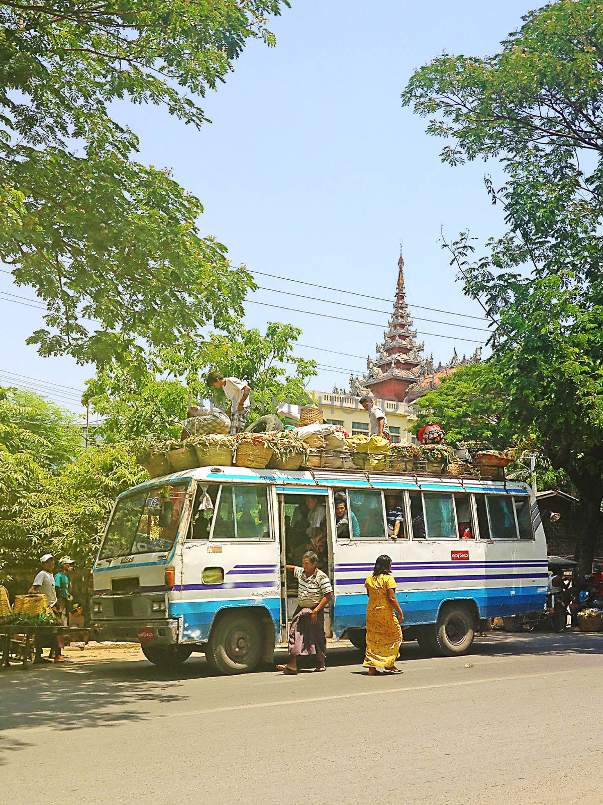 Mandalay ,Myanmar-APRIL 19,2013 : Bus, with passengers on roof,under trees and  pagoda background