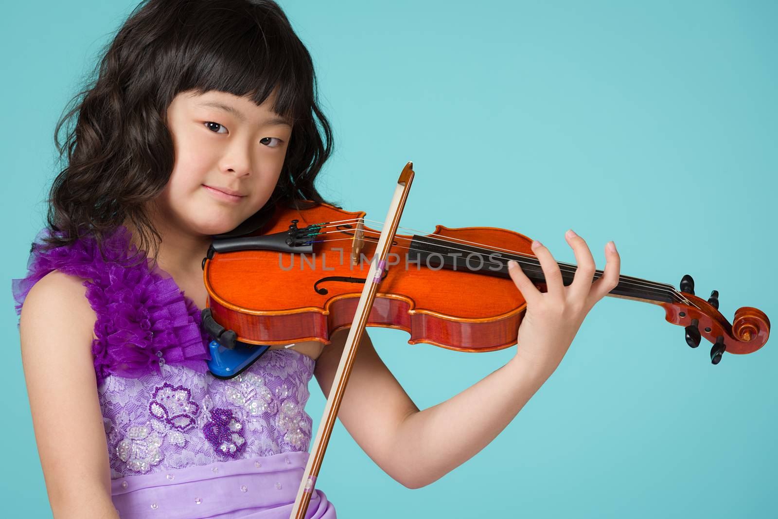 A portrait of a cute, happy and young Japanese girl in a purple dress on a blue background with a violin.