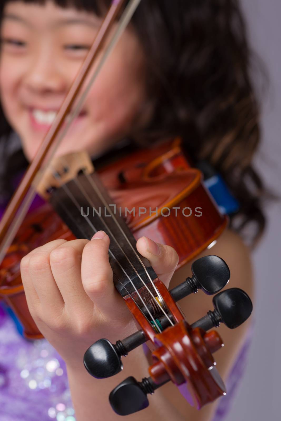 A portrait of a cute, happy and young Japanese girl in a purple dress with a violin with the focus on her hand instead of her face.