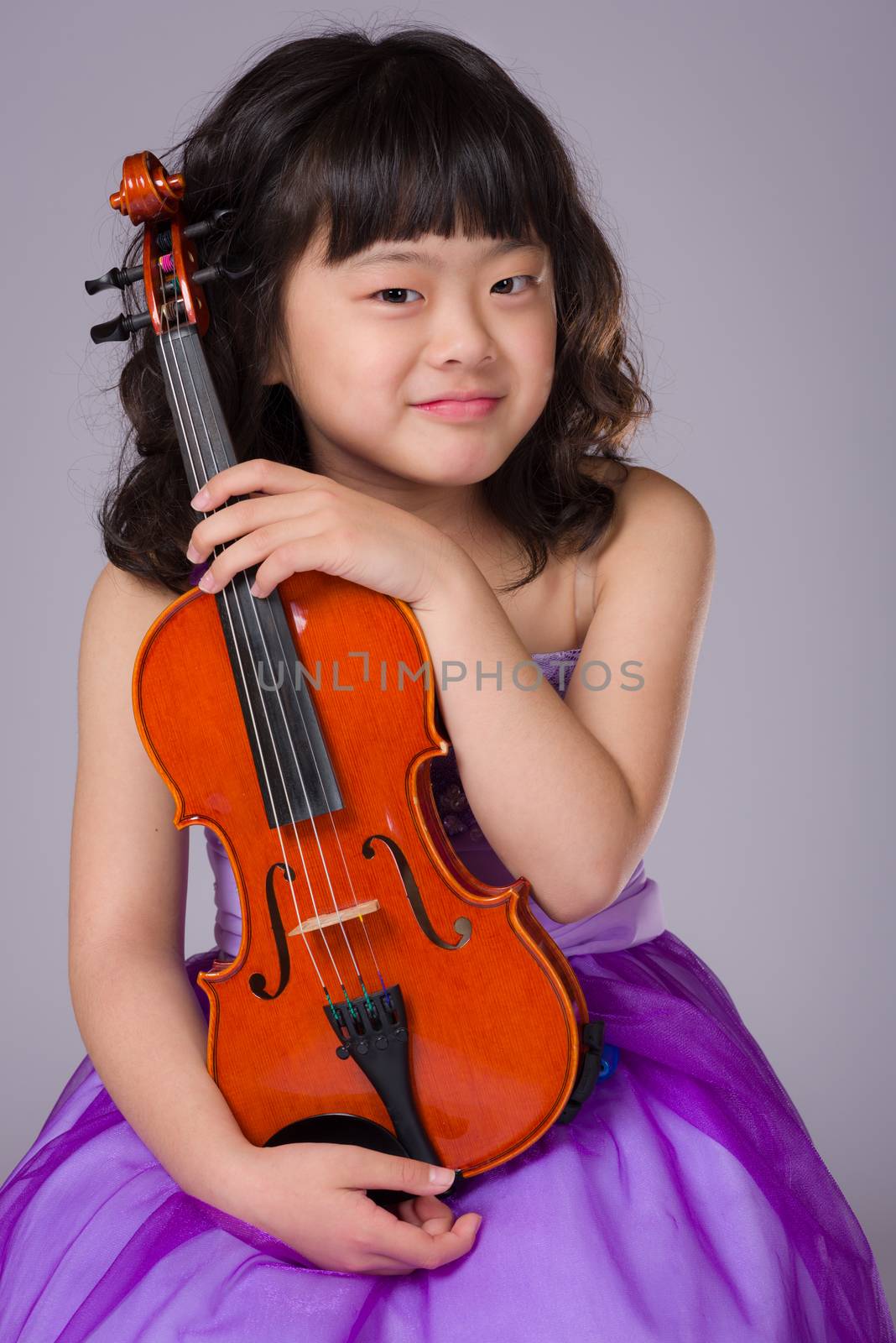A portrait of a cute, happy and young Japanese girl in a purple dress on a grey background with a violin.