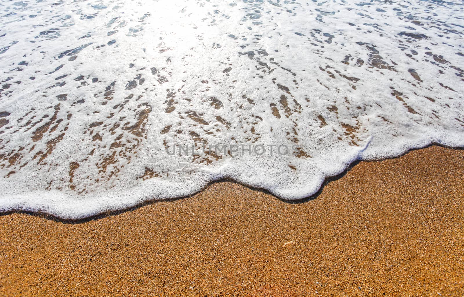 Sun light reflected on soft wave of the sea on the sandy beach