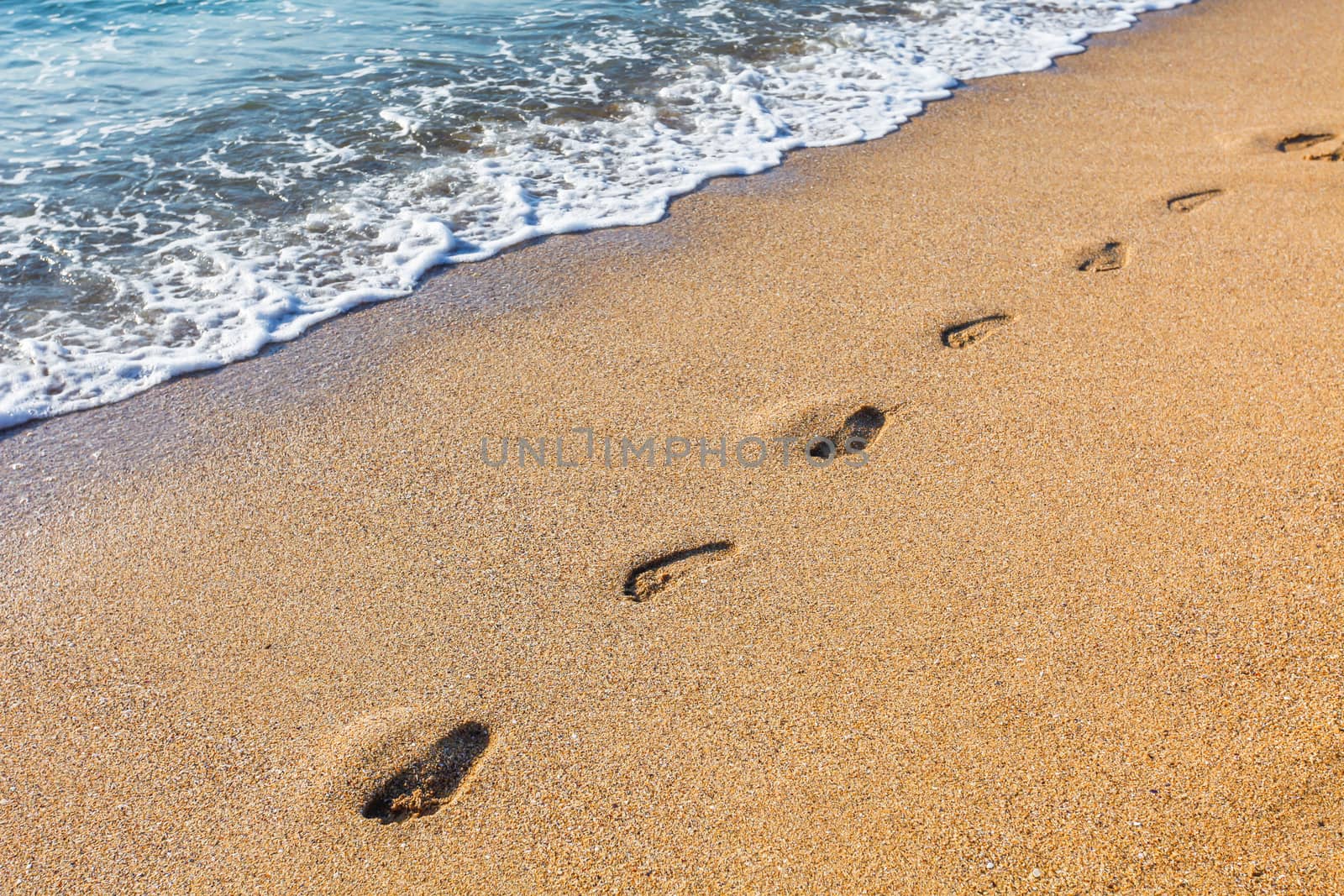 Footmarks on the sandy beach with soft wave of the sea