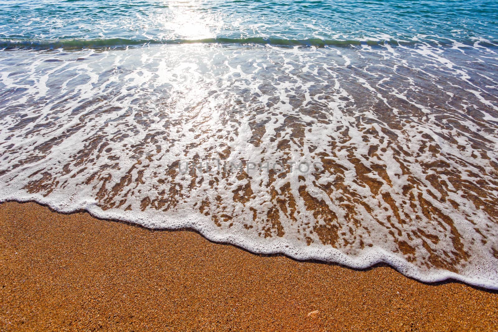 Sun light reflected on soft wave of the sea on the sandy beach