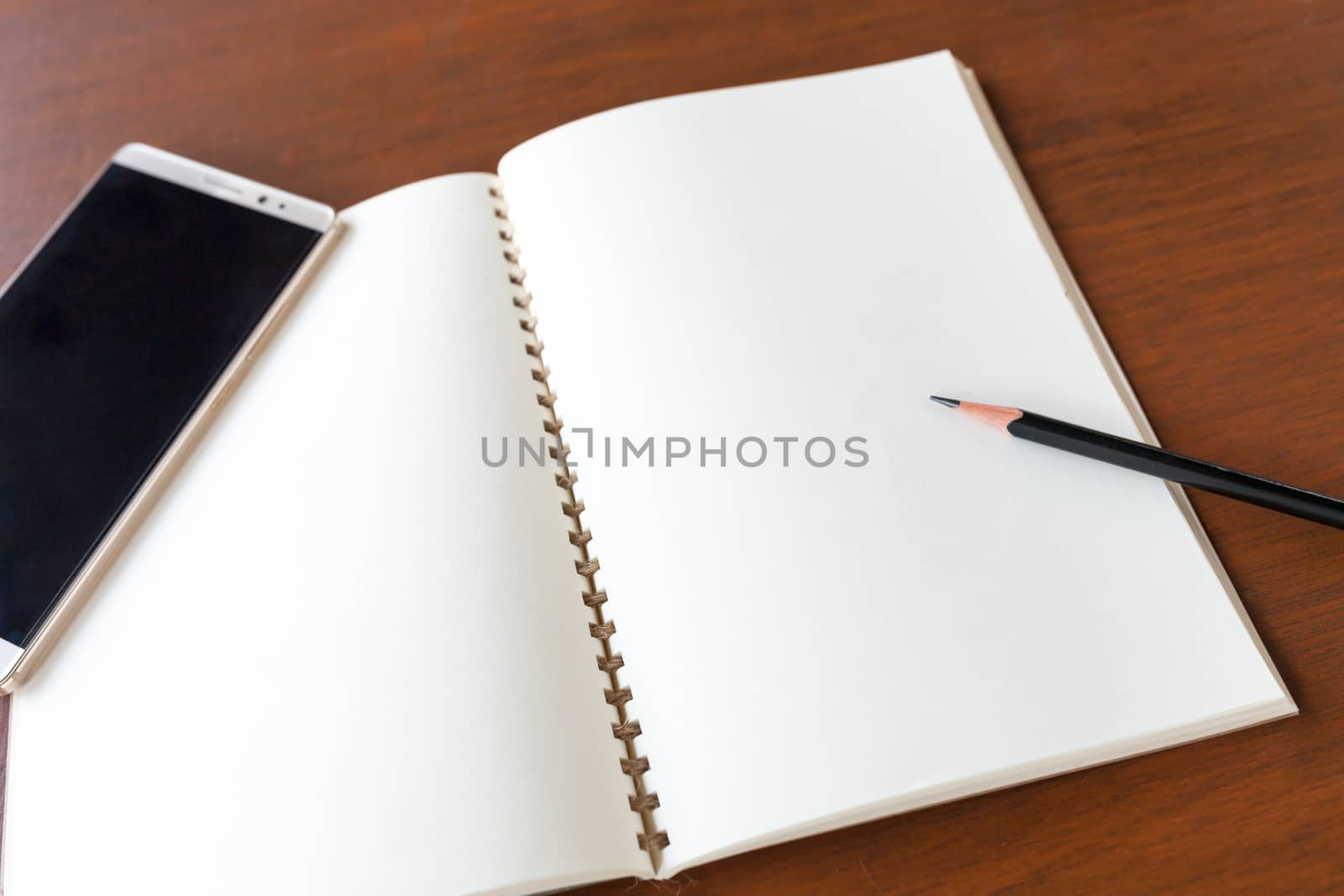 Blank note book with pencil and smartphone on wooden table background concept and Idea for write your text here.