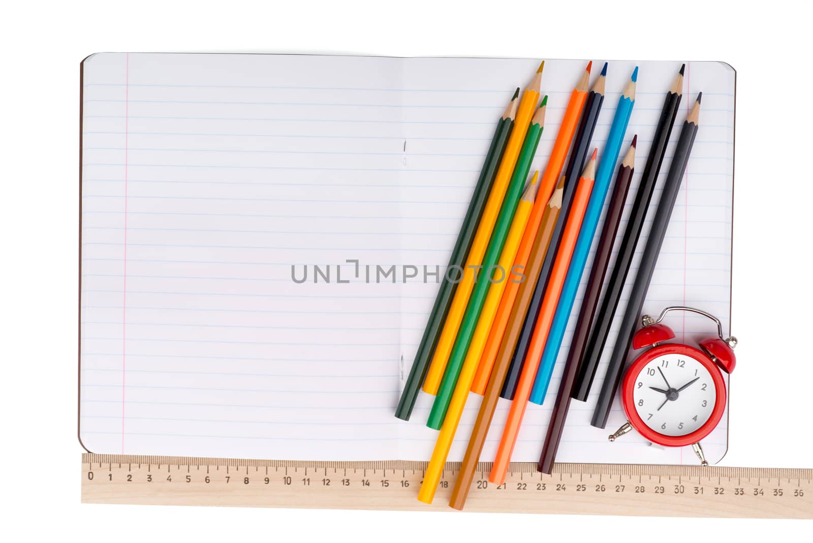 Open notebook with crayons, ruler and alarm clock on isolated white background, closeup