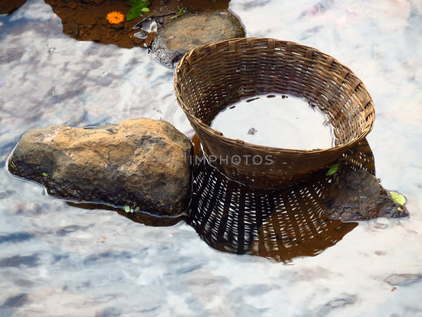 An empty cane basket abandoned on the rocks near a river stream 