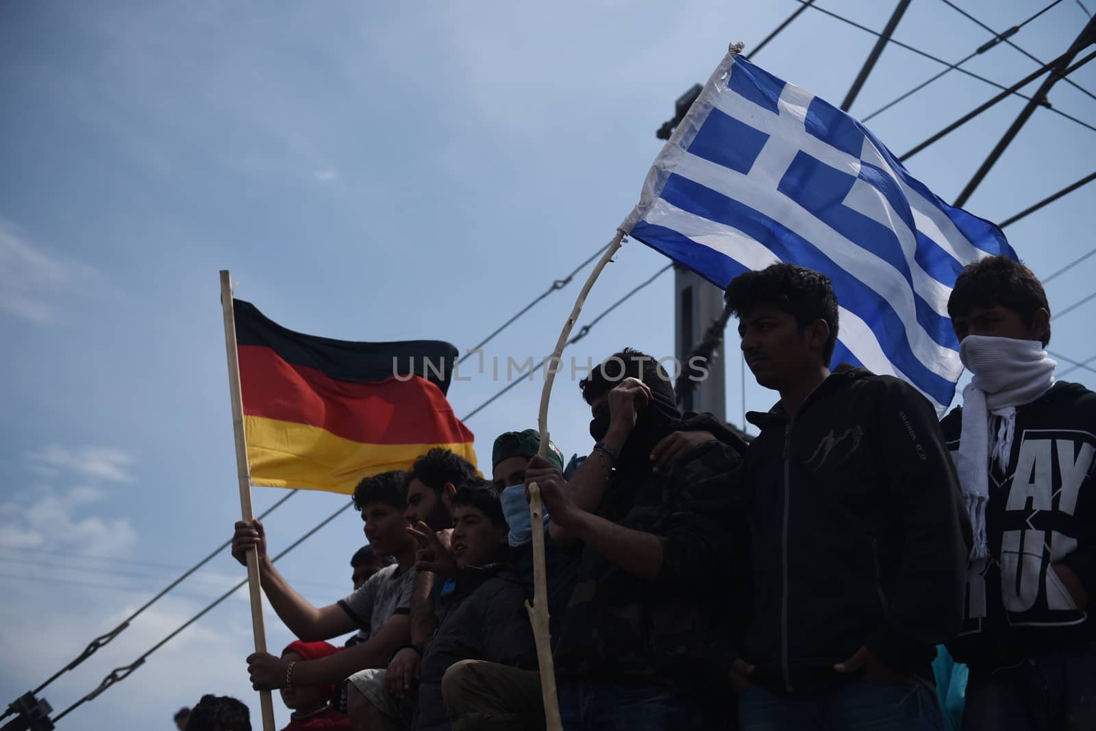 GREECE, Idomeni: Migrants hold up the Greek and German flags near the Macedonia-Greek border on April 11, 2016.Hundreds of migrants were injured on Sunday as they attempted to cross the border into Macedonia. Police used tear gas, water cannons, and stun grenades to disperse the crowd as migrants threw stones in retaliation. 