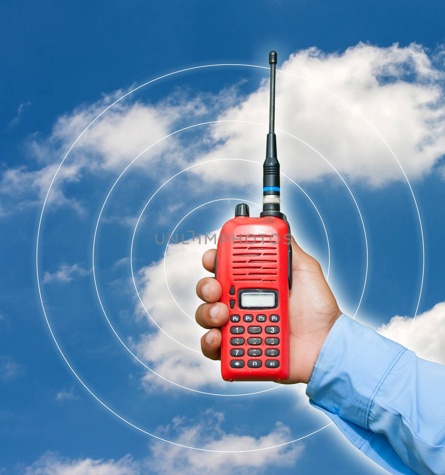 Red portable radio transceiver in hand on blue sky
