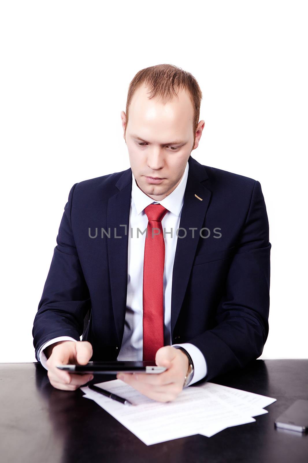 Serious American Businessman in red tie at the table working on the tablet. Isolated on white background