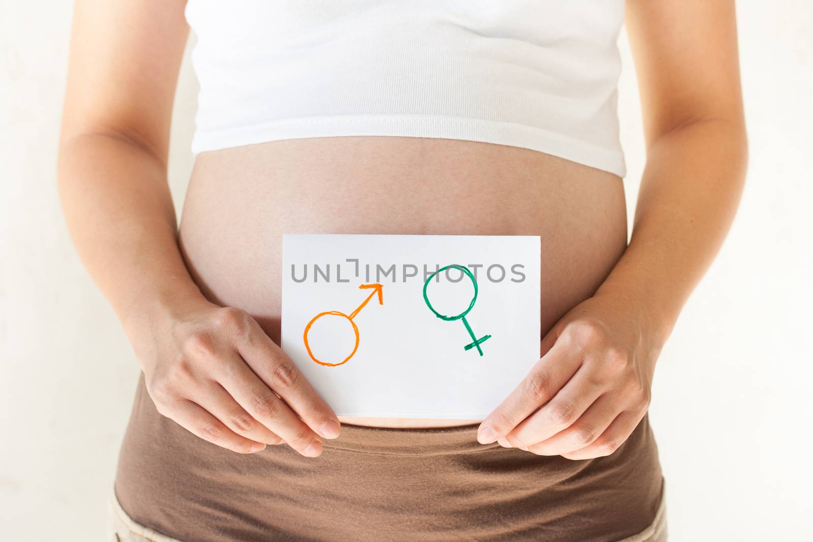 Pregnant woman holding her hands on the belly and holding a paper with symbols are boy and girl