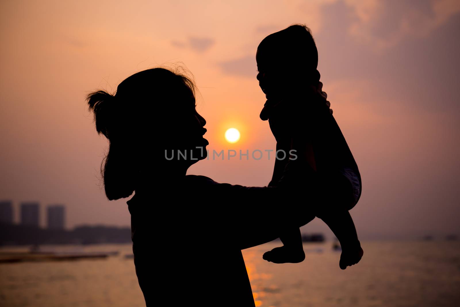 Silhouette of mother plays with her toddler against the sunset. by pkproject