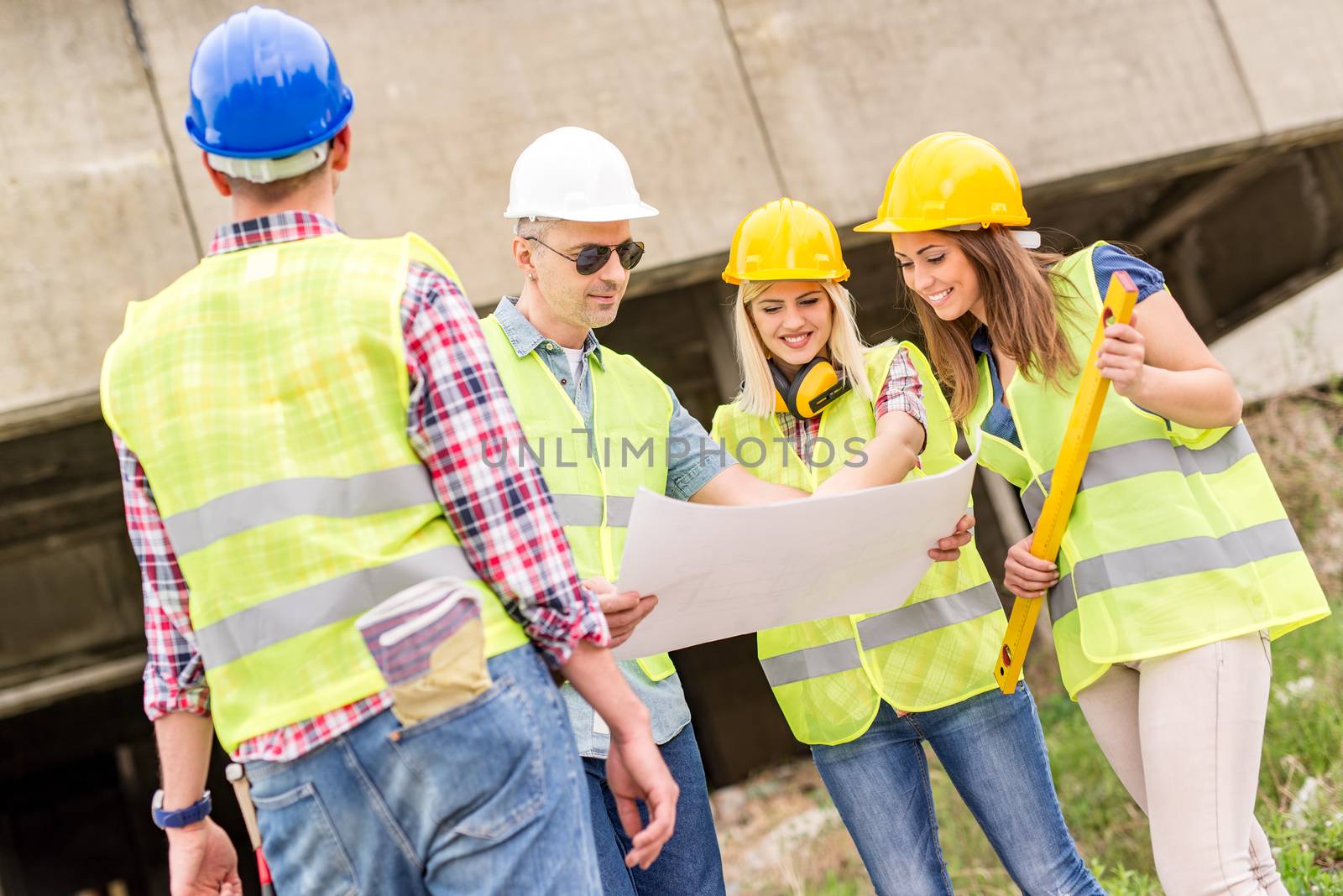 Four construction architects review plan at a construction site.