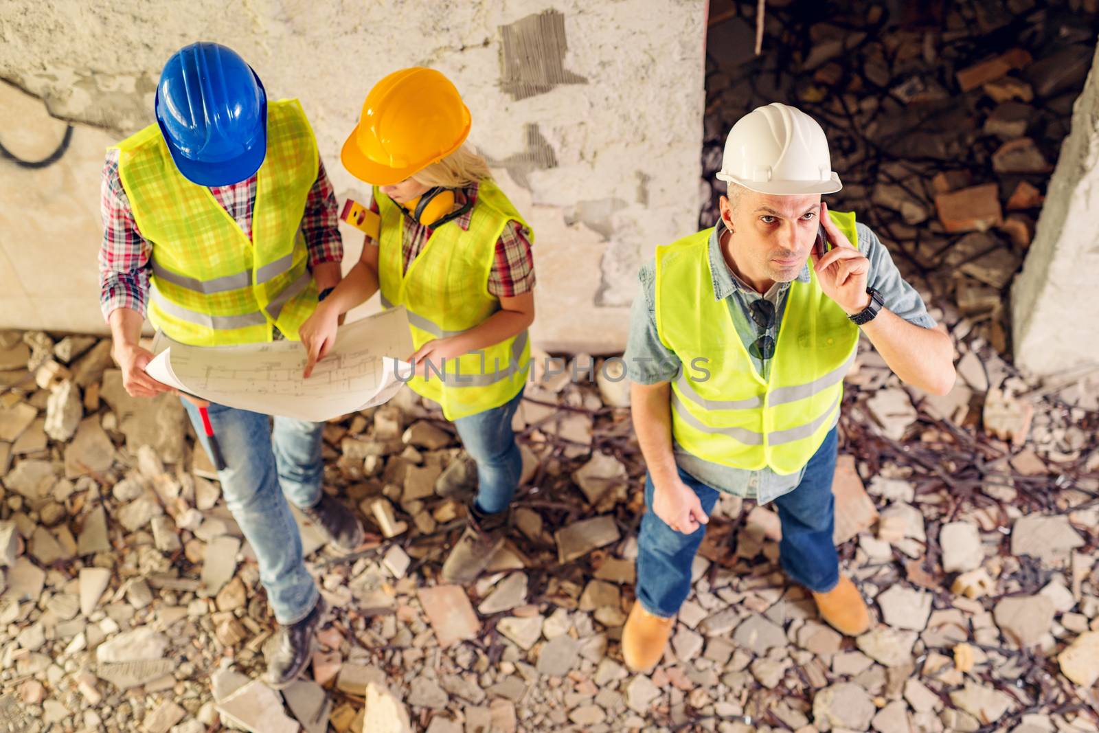 Construction architects using phone in building damaged in the disaster. His colleagues review plan.