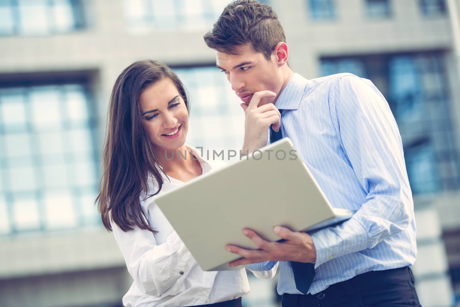 Close-up of a young business partners standing in front of office building and looking at laptop.