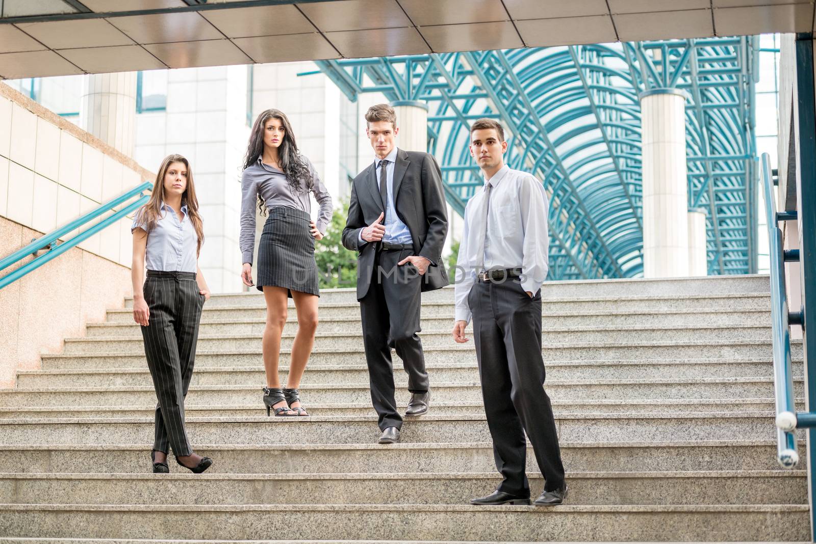 Group of young business people, elegantly dressed, standing on the steps of the company's building.