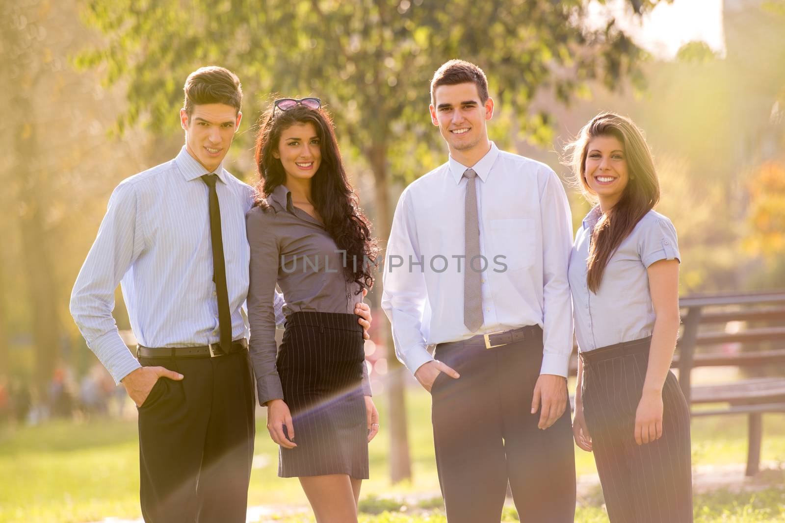 Small group of business people, elegantly dressed, standing in the park, looking at the camera, enjoying the sunny day.