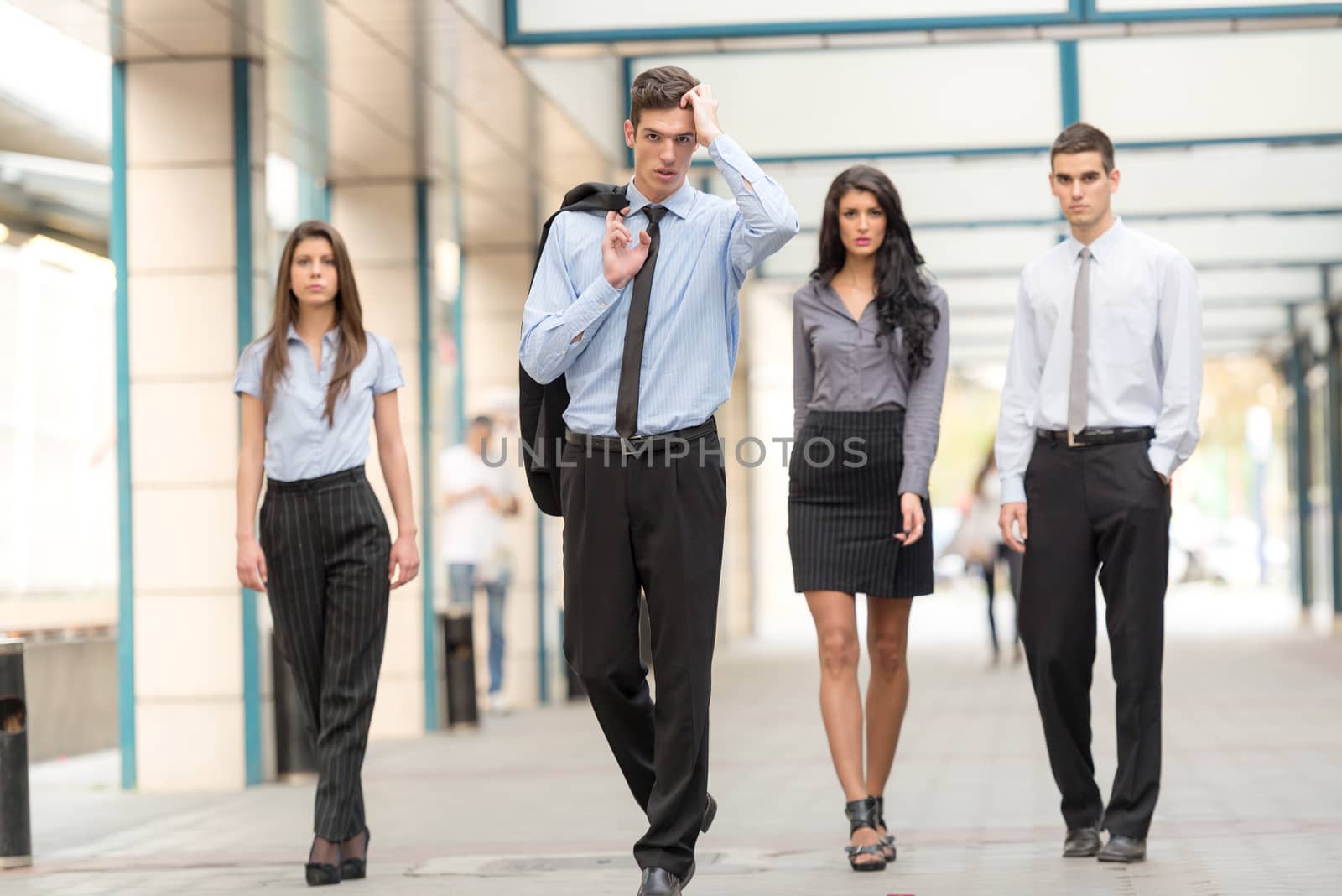 A small group of young business people, elegantly dressed, pass through the passage office building, looking at the camera with serious expressions on their faces