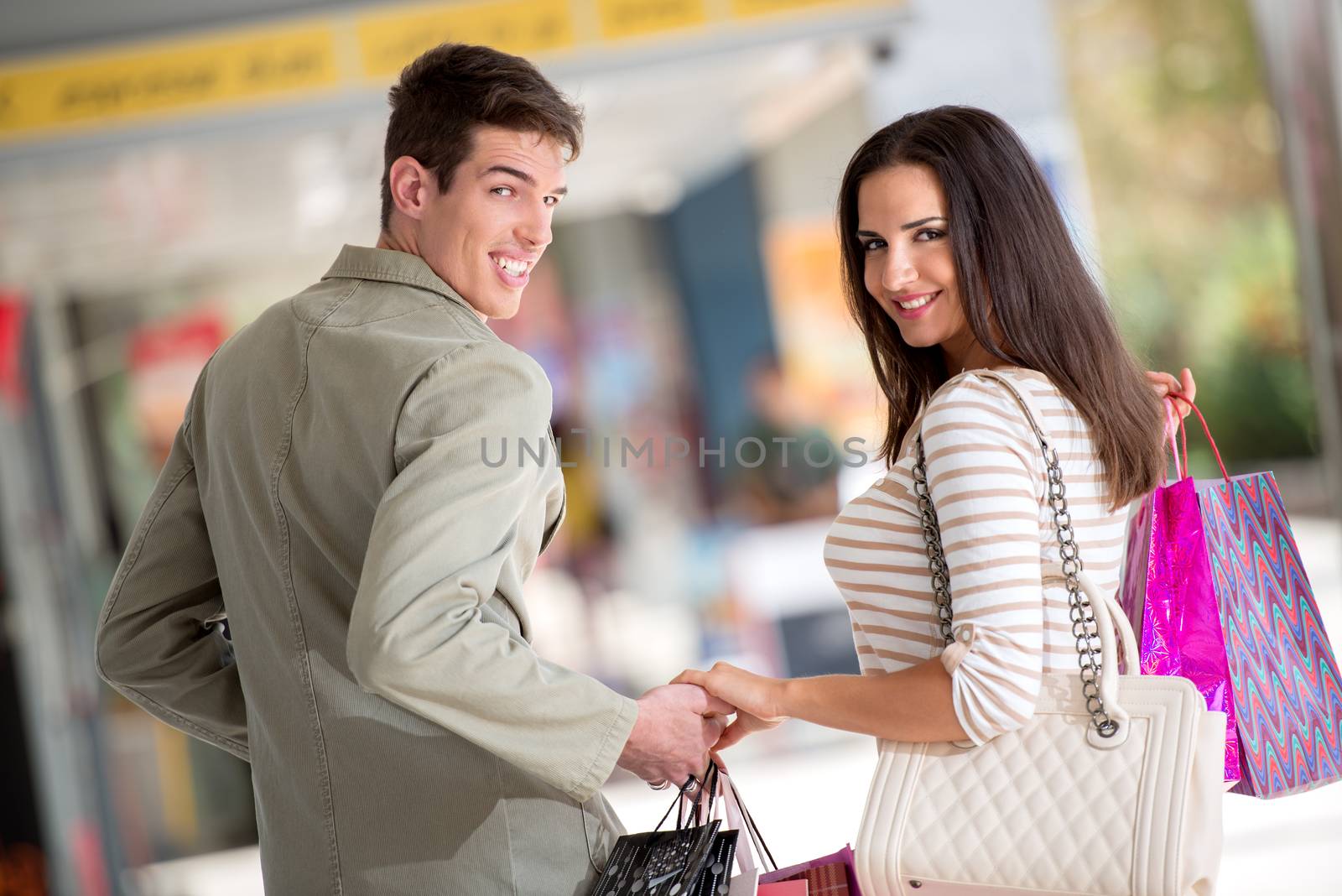 Close-up of a beautiful couple passing through town after shopping, carrying a bunch of shopping bags, looking at camera behind their back.