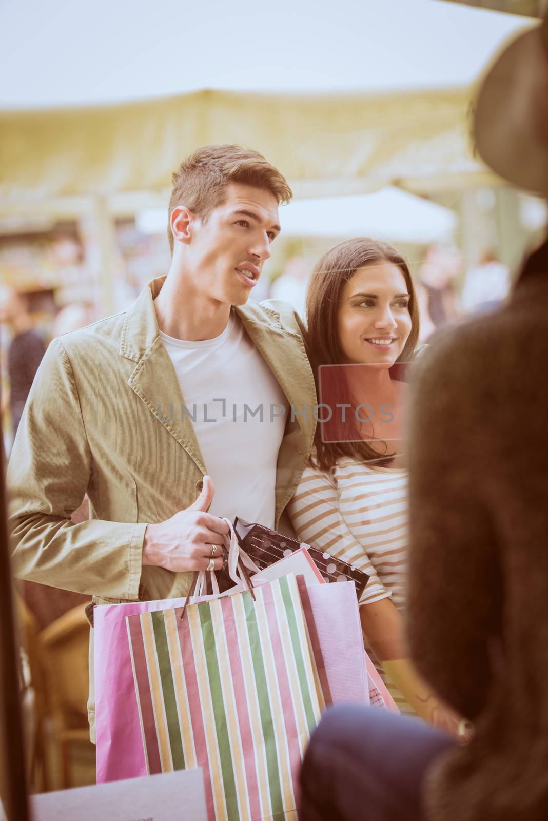 Young happy couple in shopping passes in front of window shopping mall carrying bags in their hands, looking in shop window.