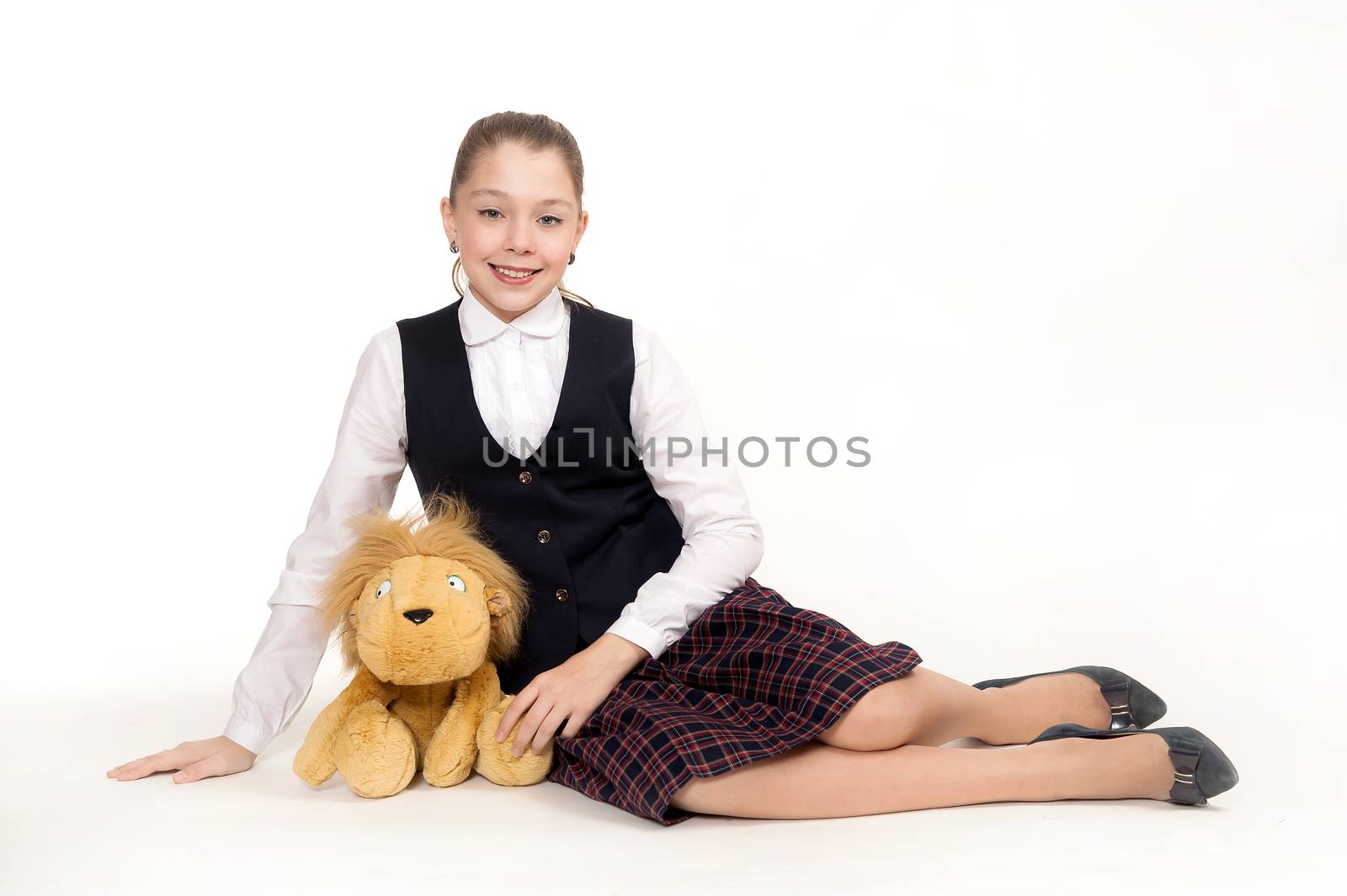 The beautiful schoolgirl sits in a school uniform and holds a toy on a white background