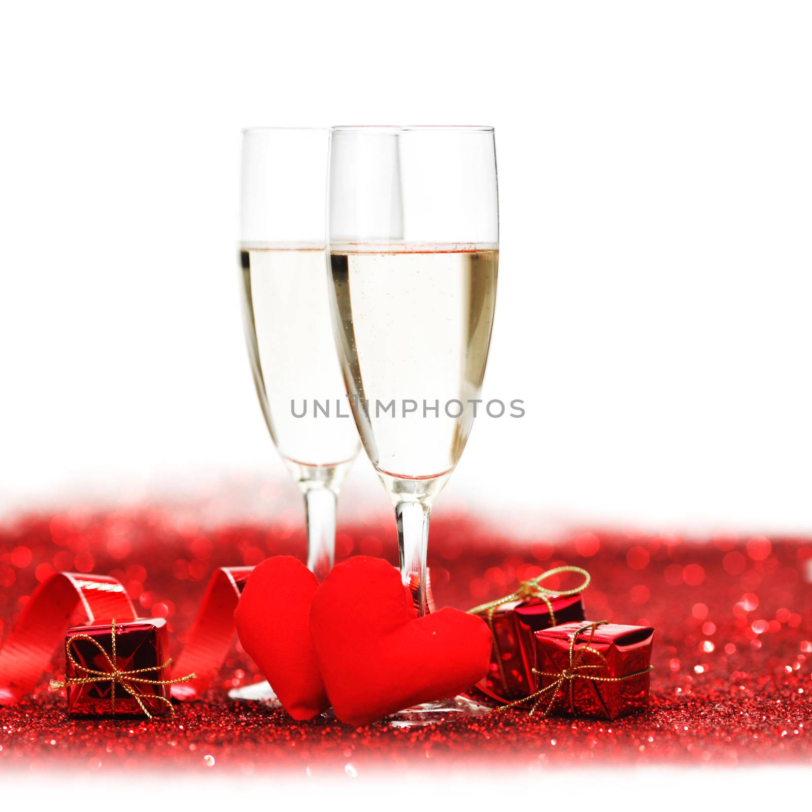 Glasses with Champagne and handmade hearts on red glitters isolated on white background