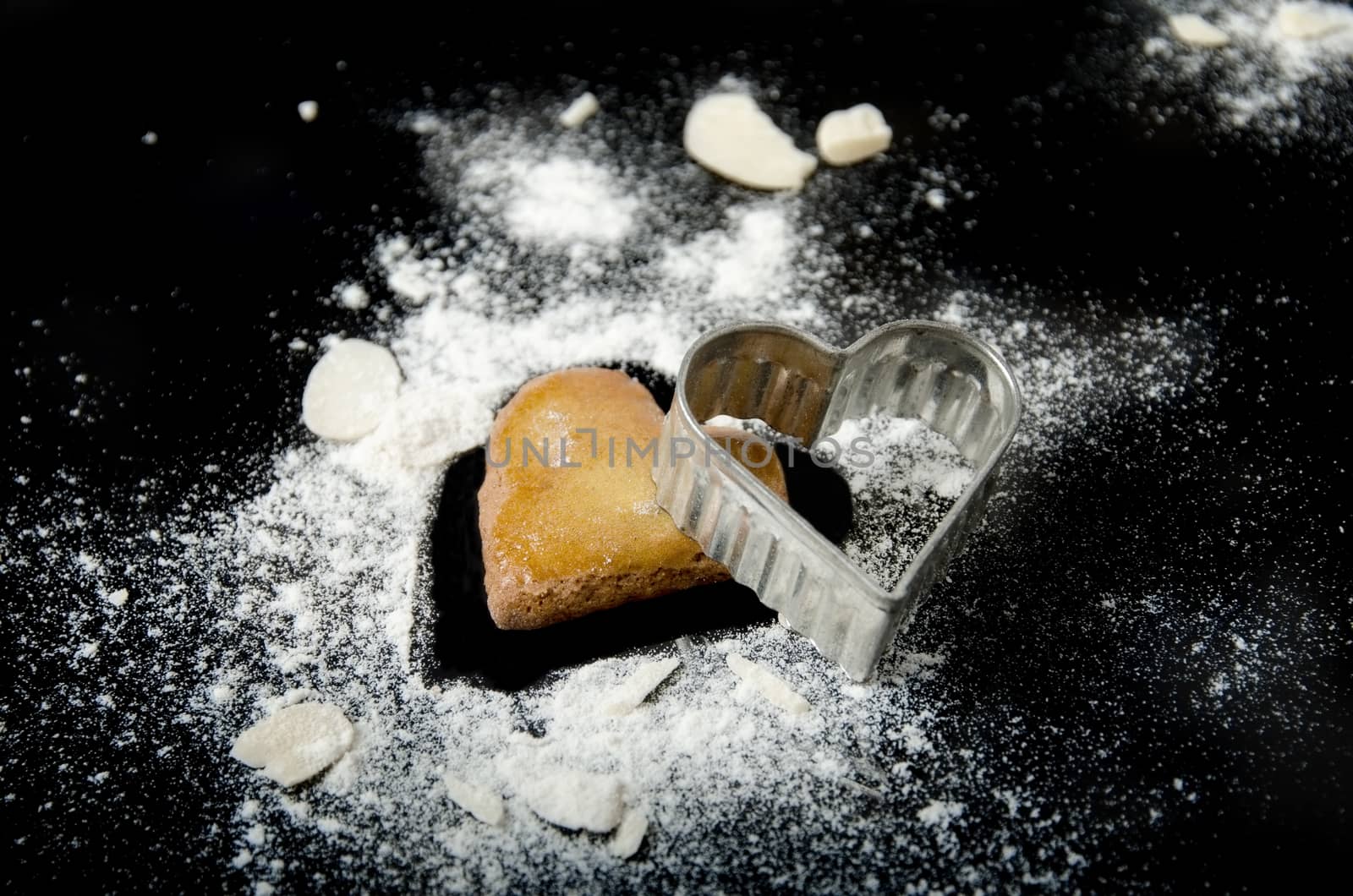 Gingerbread heart still life with almond and flour isolated on black background.