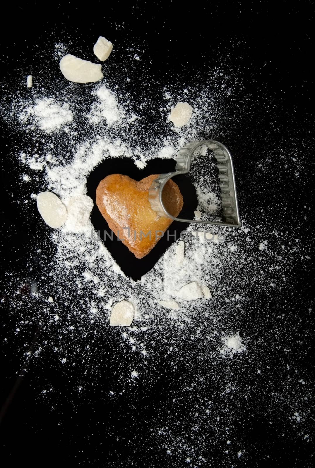 Gingerbread heart and cutter with almond and flour isolated on black background.