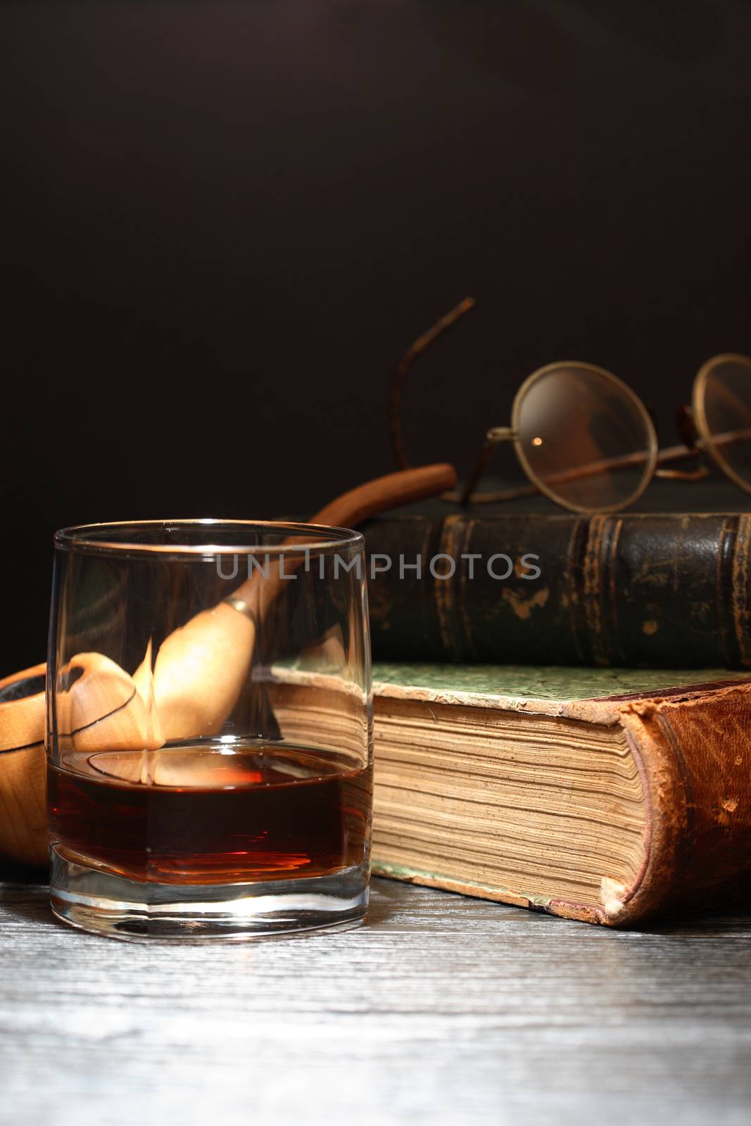 Glass of whiskey near old books on dark background 