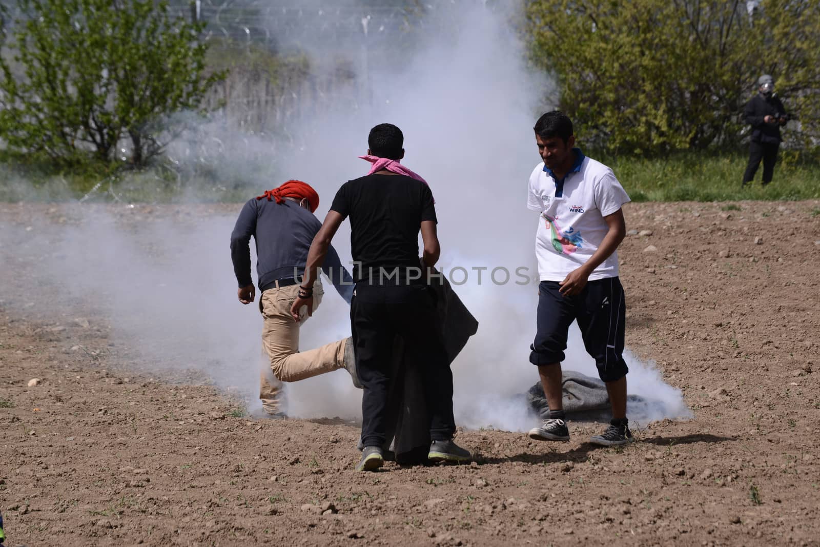 GREECE, Idomeni: A man throws back to macedonian police a tear gas shell as migrants and refugees tried to break down the border fence near their makeshift camp at the Greek-Macedonian border near Idomeni village, on April 13, 2016. About 100 migrants spread out over about 100 metres (yards) tugging at the wire fence, but swiftly pulled back when two squads of Greek riot police moved in, the reporter said. The Greek riot police positioned themselves between the migrants and the Macedonian fence, ending the incident.
