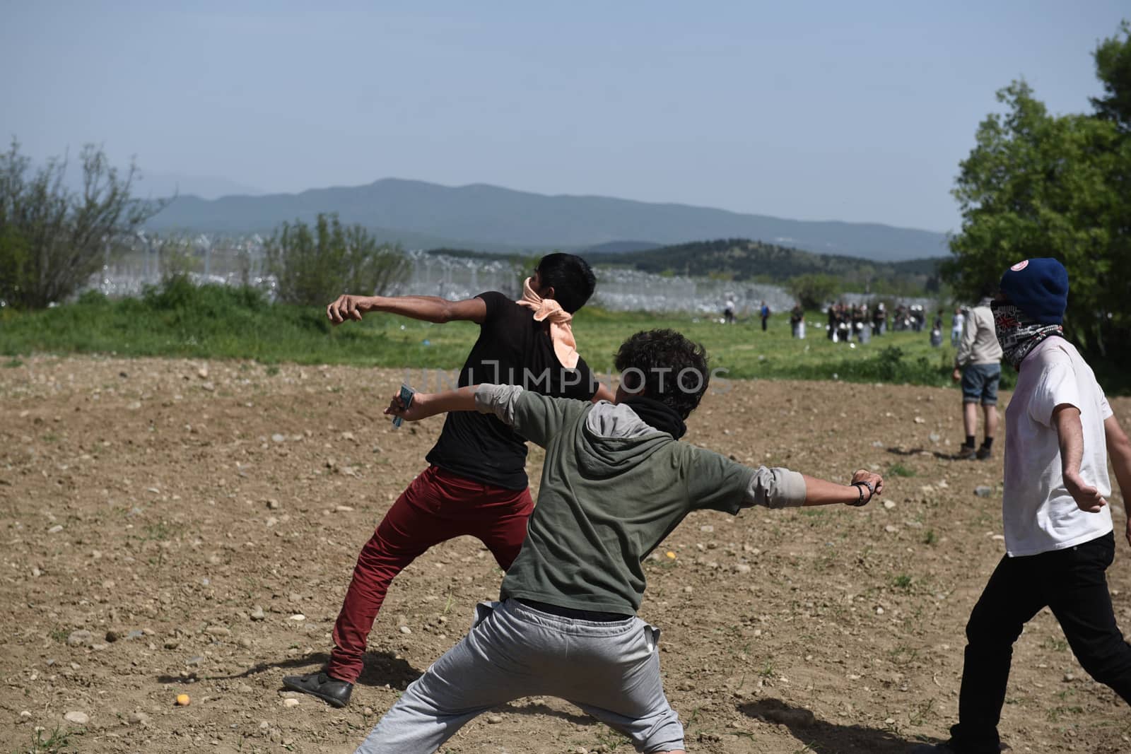 GREECE, Idomeni: Two men throw stones back to macedonian police that fired tear gas as migrants and refugees tried to break down the border fence near their makeshift camp at the Greek-Macedonian border near Idomeni village, on April 13, 2016. About 100 migrants spread out over about 100 metres (yards) tugging at the wire fence, but swiftly pulled back when two squads of Greek riot police moved in, the reporter said. The Greek riot police positioned themselves between the migrants and the Macedonian fence, ending the incident.