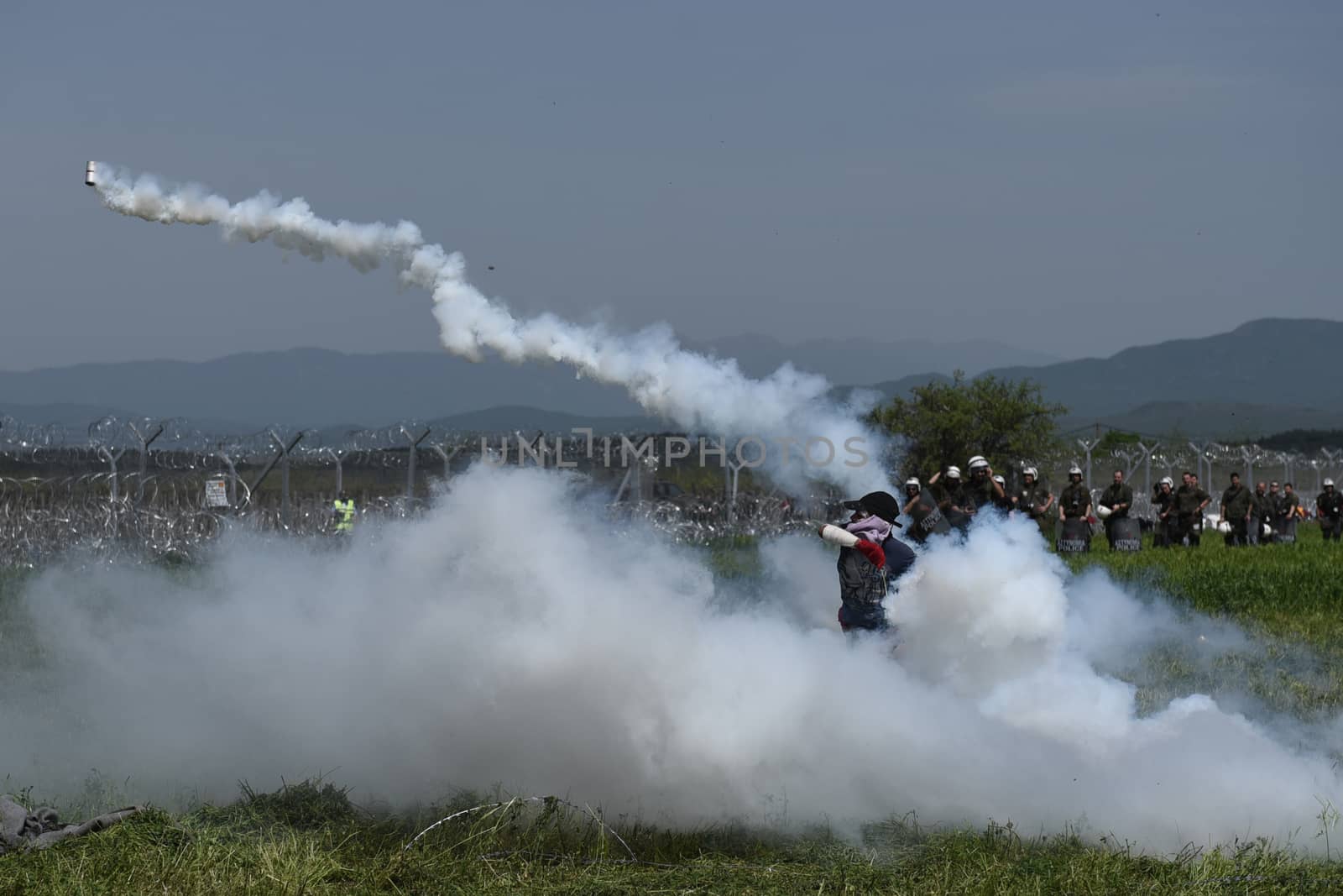 GREECE, Idomeni: A man throws back to Macedonian police a tear gas shell as migrants and refugees tried to break down the border fence near their makeshift camp at the Greek-Macedonian border near Idomeni village, on April 13, 2016. About 100 migrants spread out over about 100 metres (yards) tugging at the wire fence, but swiftly pulled back when two squads of Greek riot police moved in, the reporter said. The Greek riot police positioned themselves between the migrants and the Macedonian fence, ending the incident.