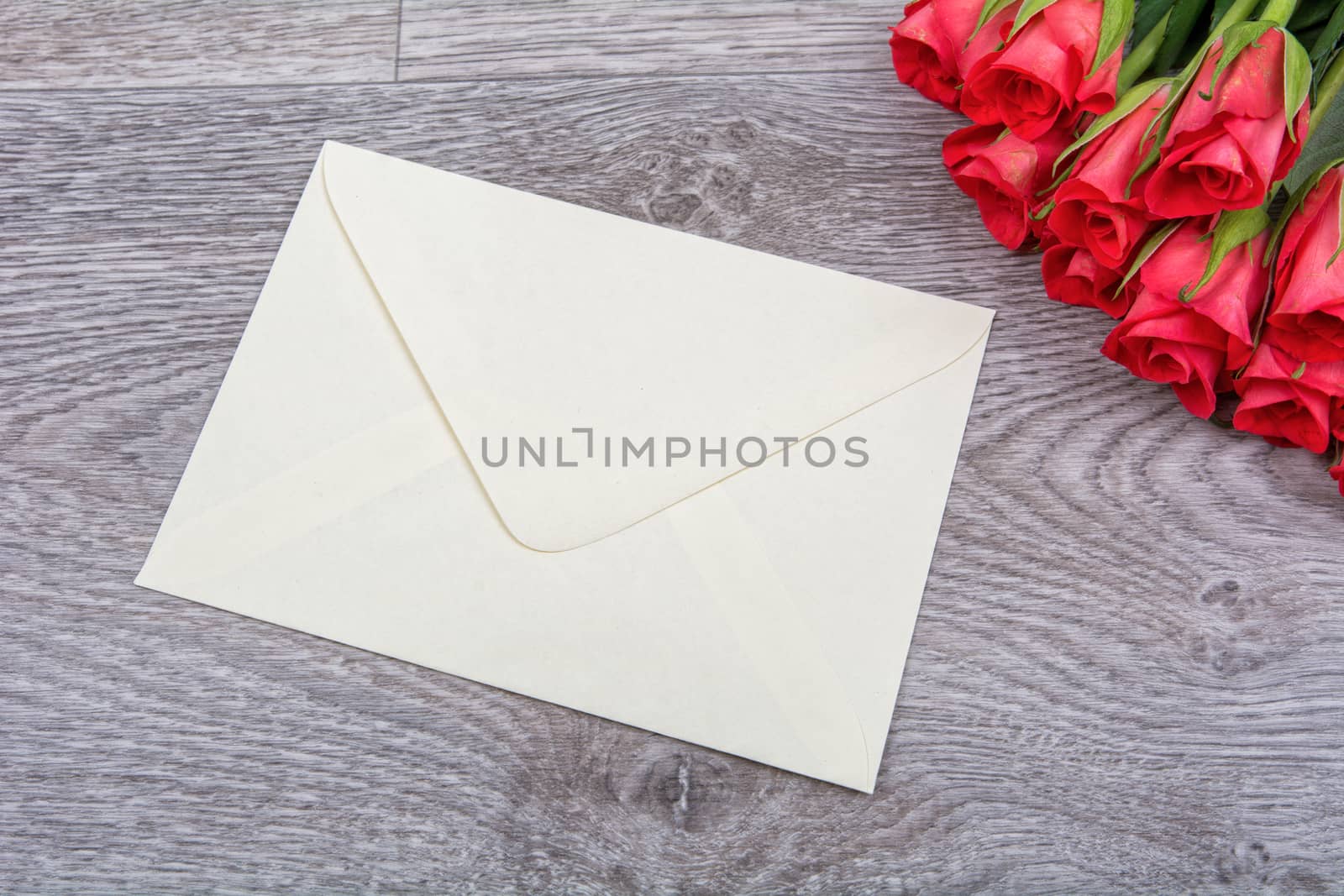 Light yellow envelope and red roses on a wooden background