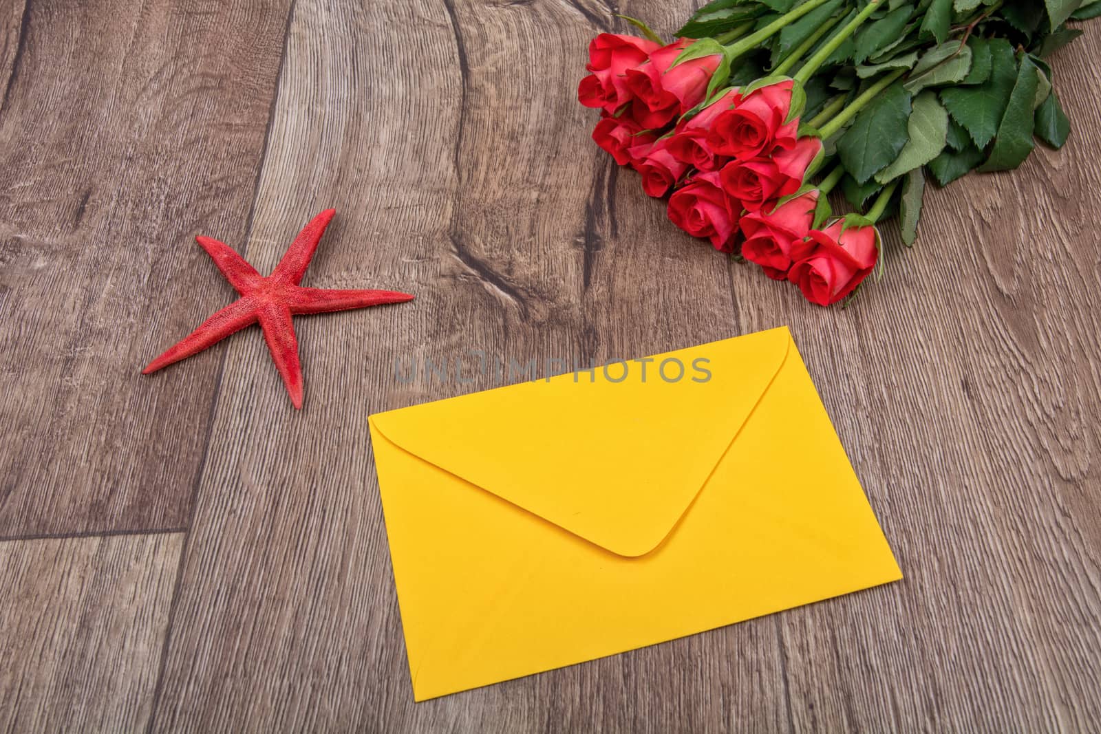 Envelope, red starfish and roses on a wooden background