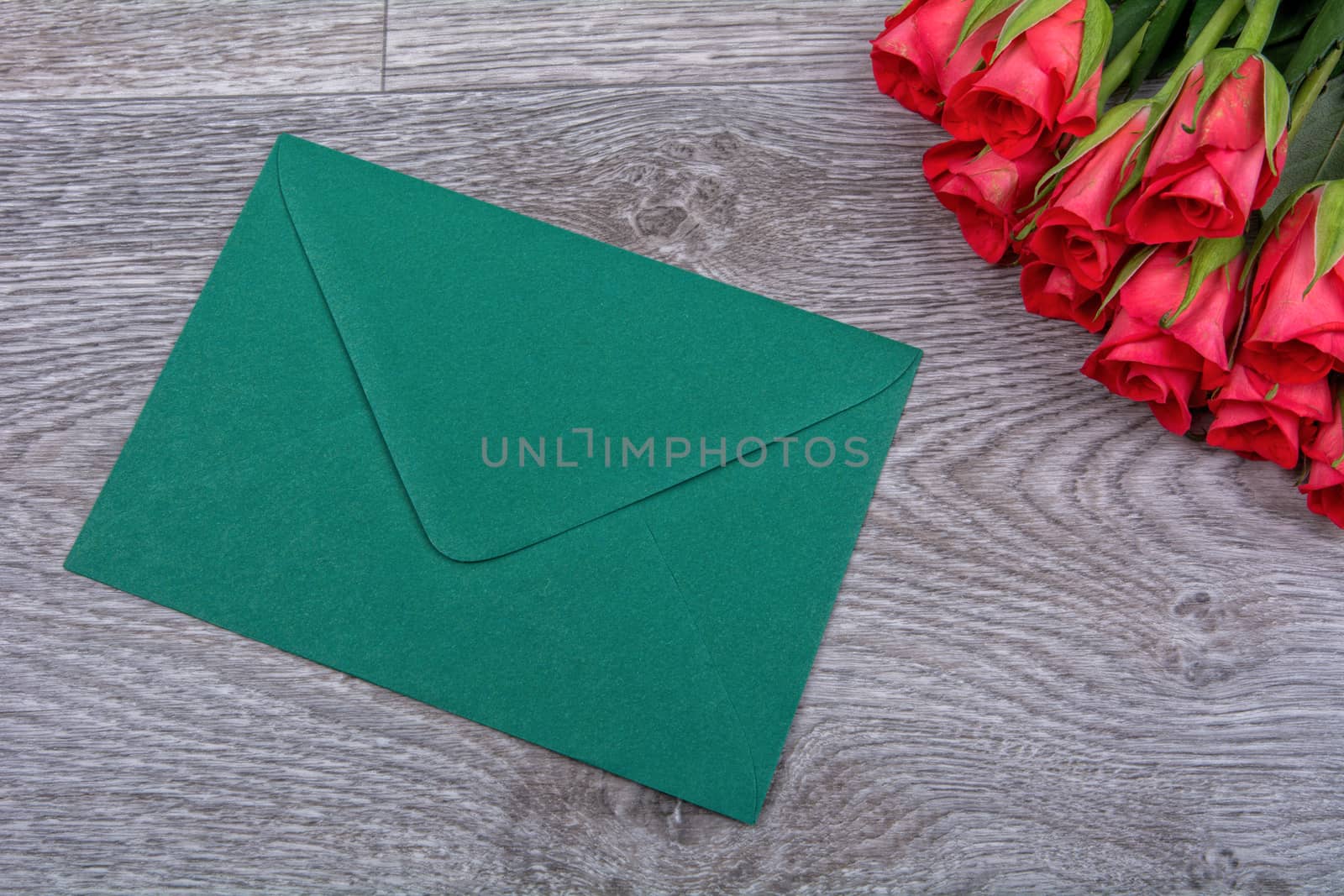 Green envelope and red roses on a wooden background