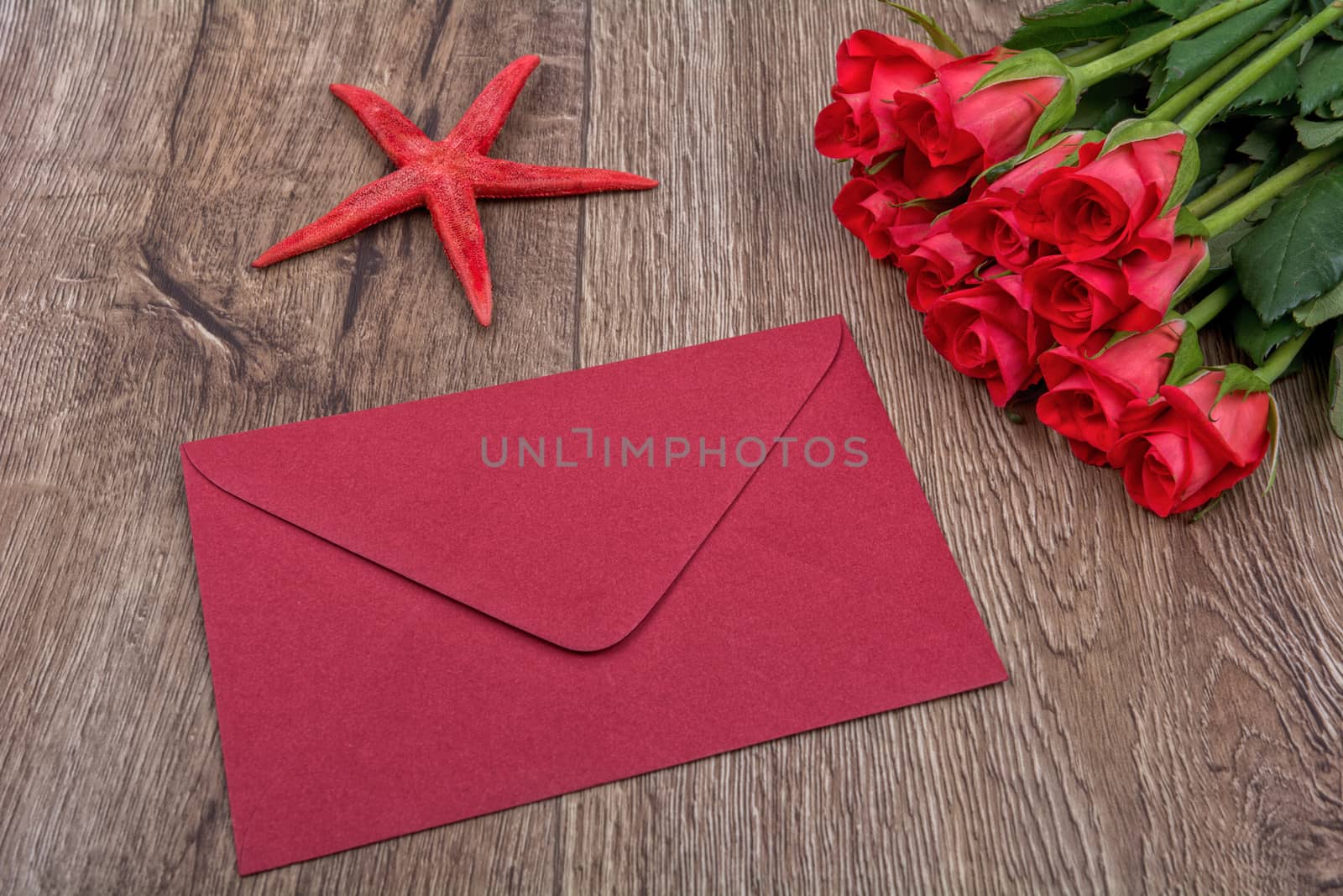 Envelope, red starfish and roses on a wooden background