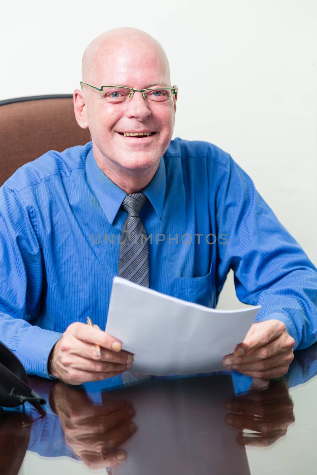 Corporate office worker at desk holding papers looking at camera