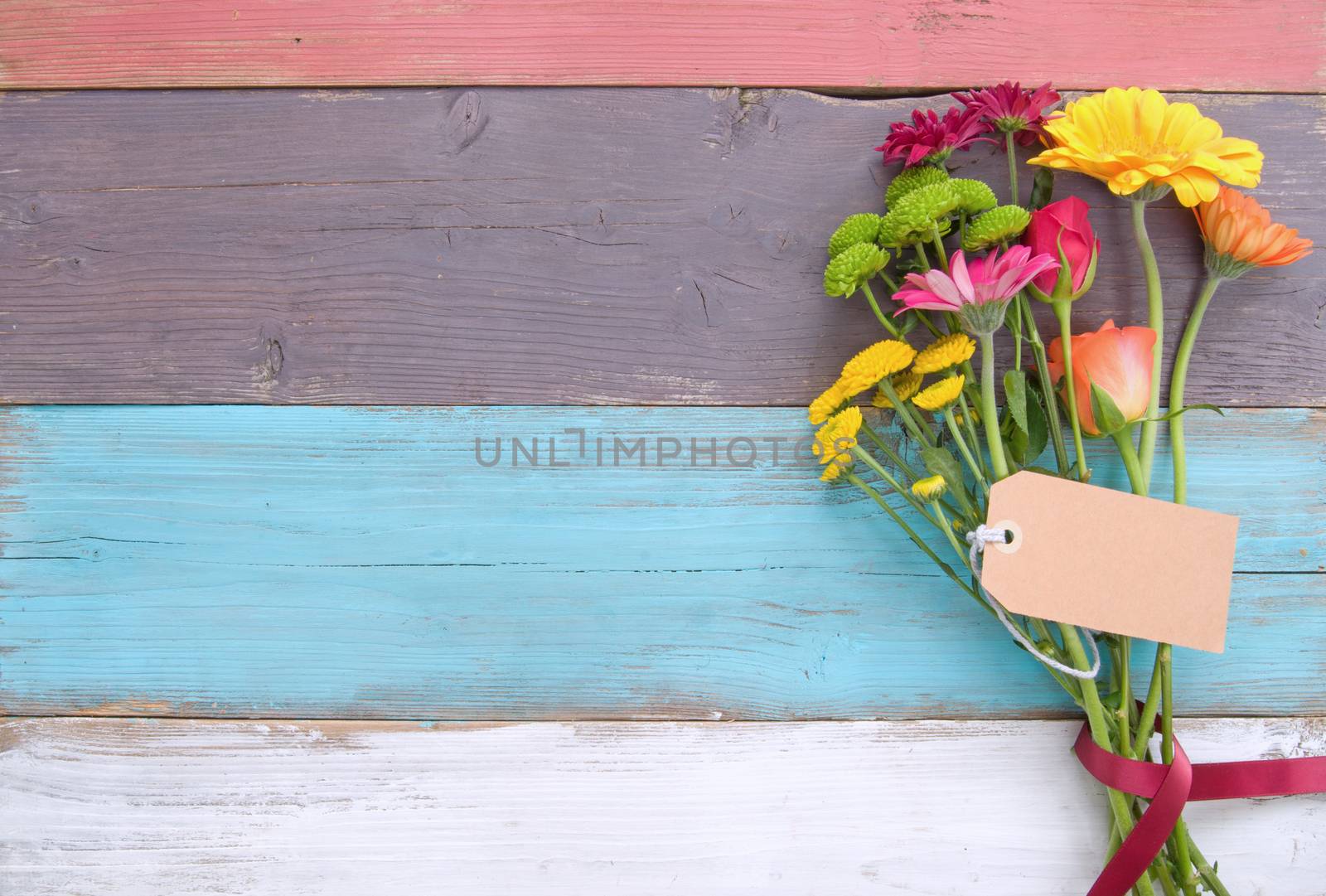 Bunch of flowers with blank gift label on wooden background