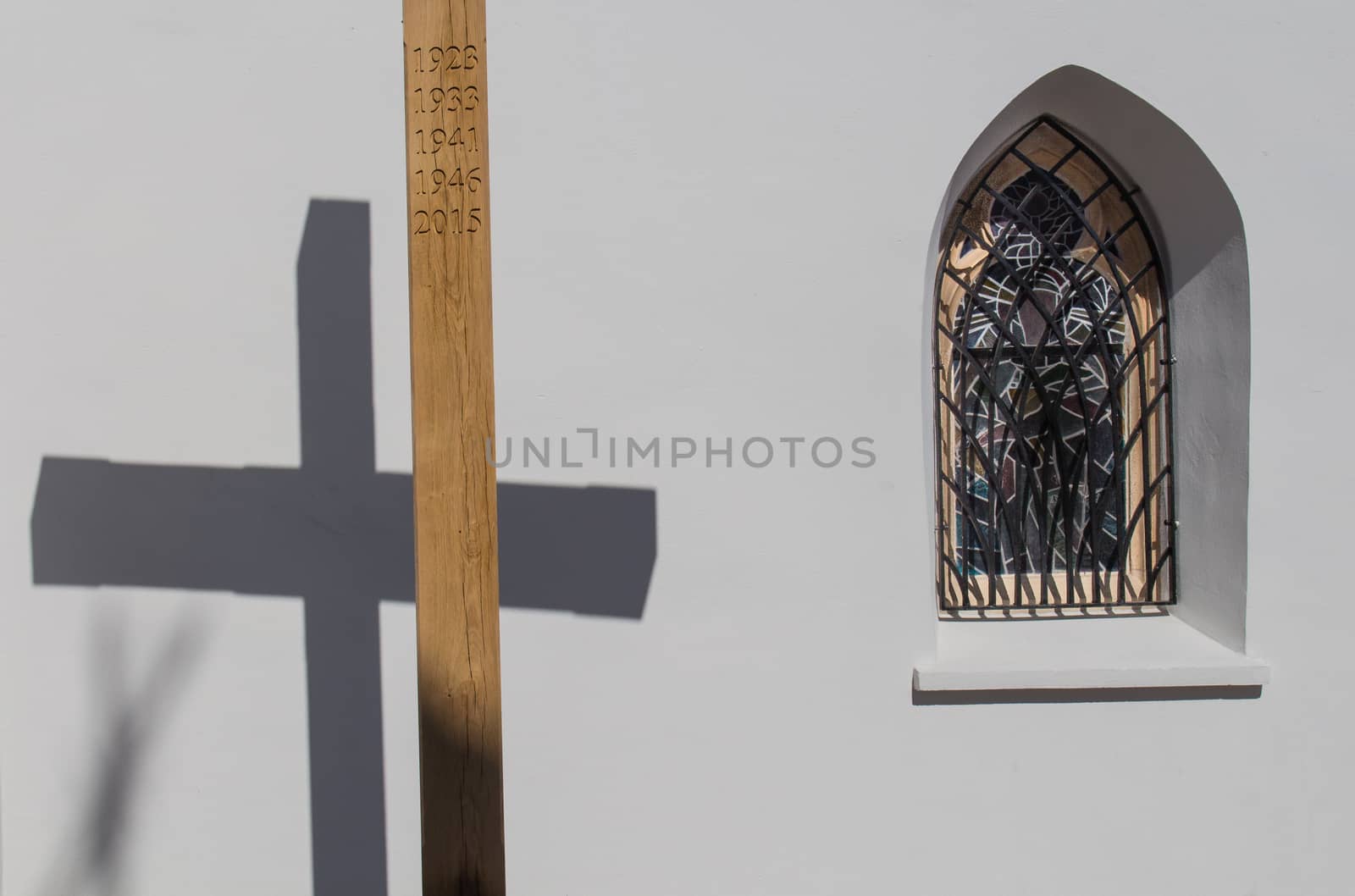 Wooden cross with a years of Saint Missions and its shadow on the wall of the gothic church in Svaty Jur, Slovakia. Traditional gothic window beside.