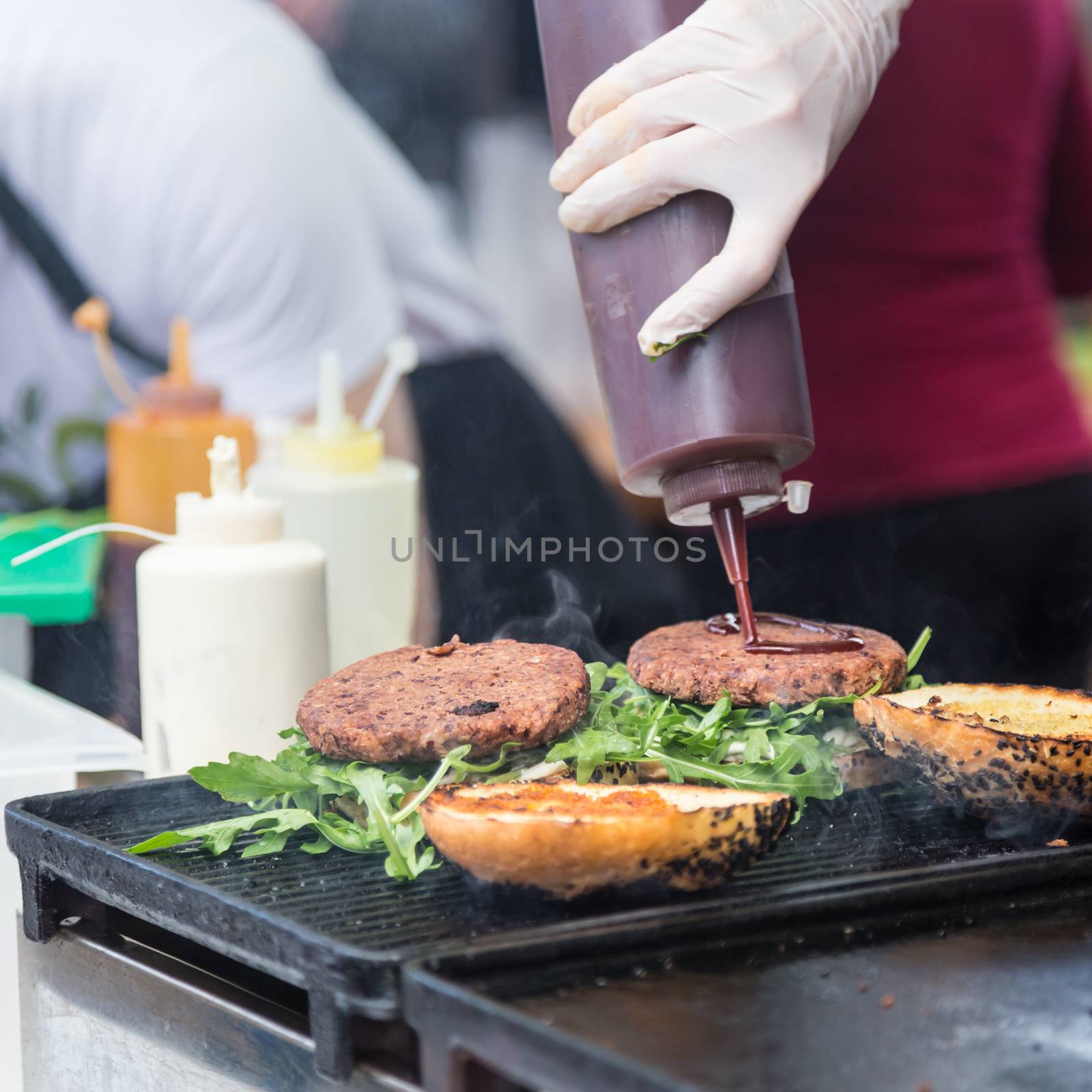 Chef making beef burgers outdoor on open kitchen international food festival event. Street food ready to serve on a food stall.