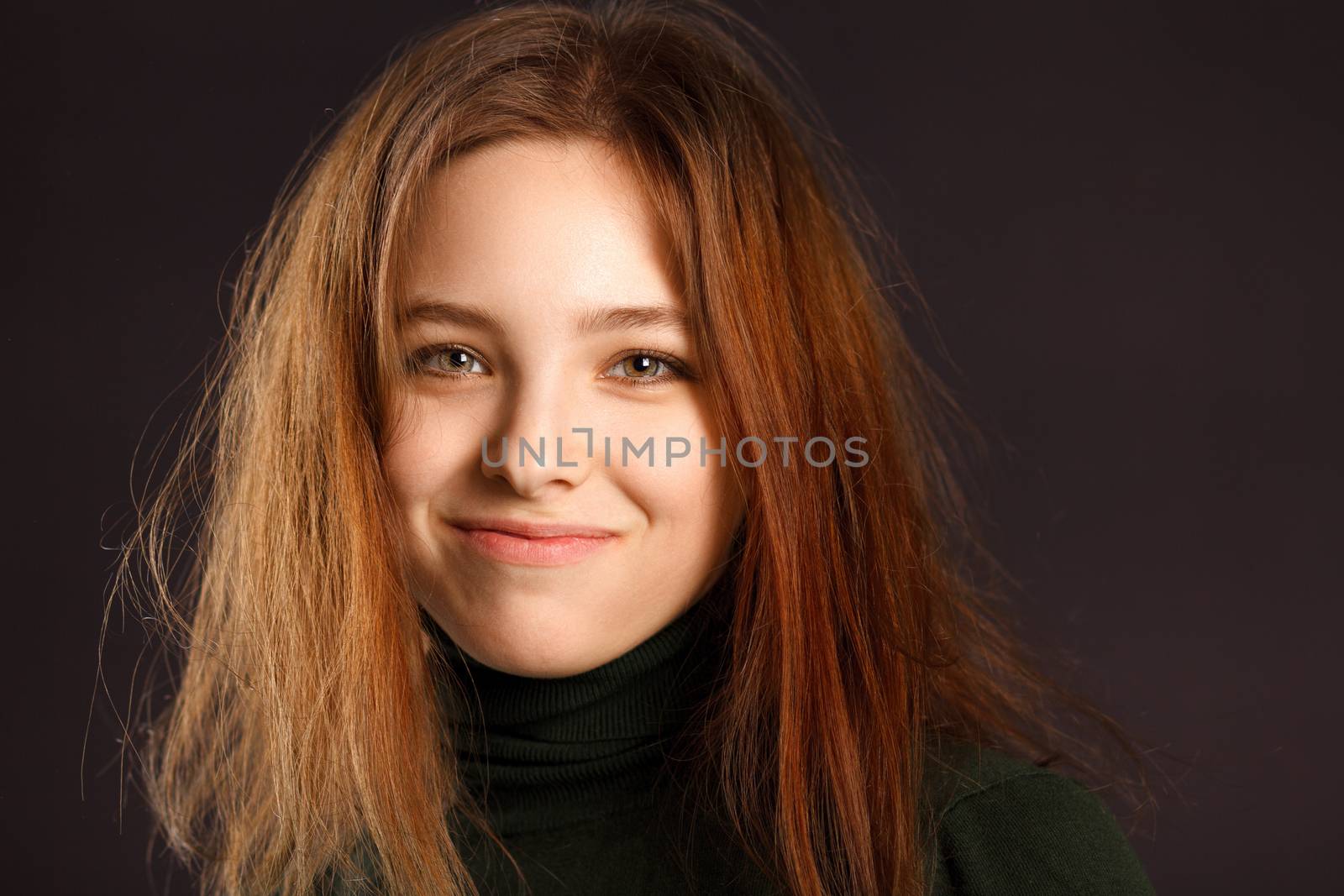 Closeup portrait of cute smiling redhead woman with disheveled hair on dark background