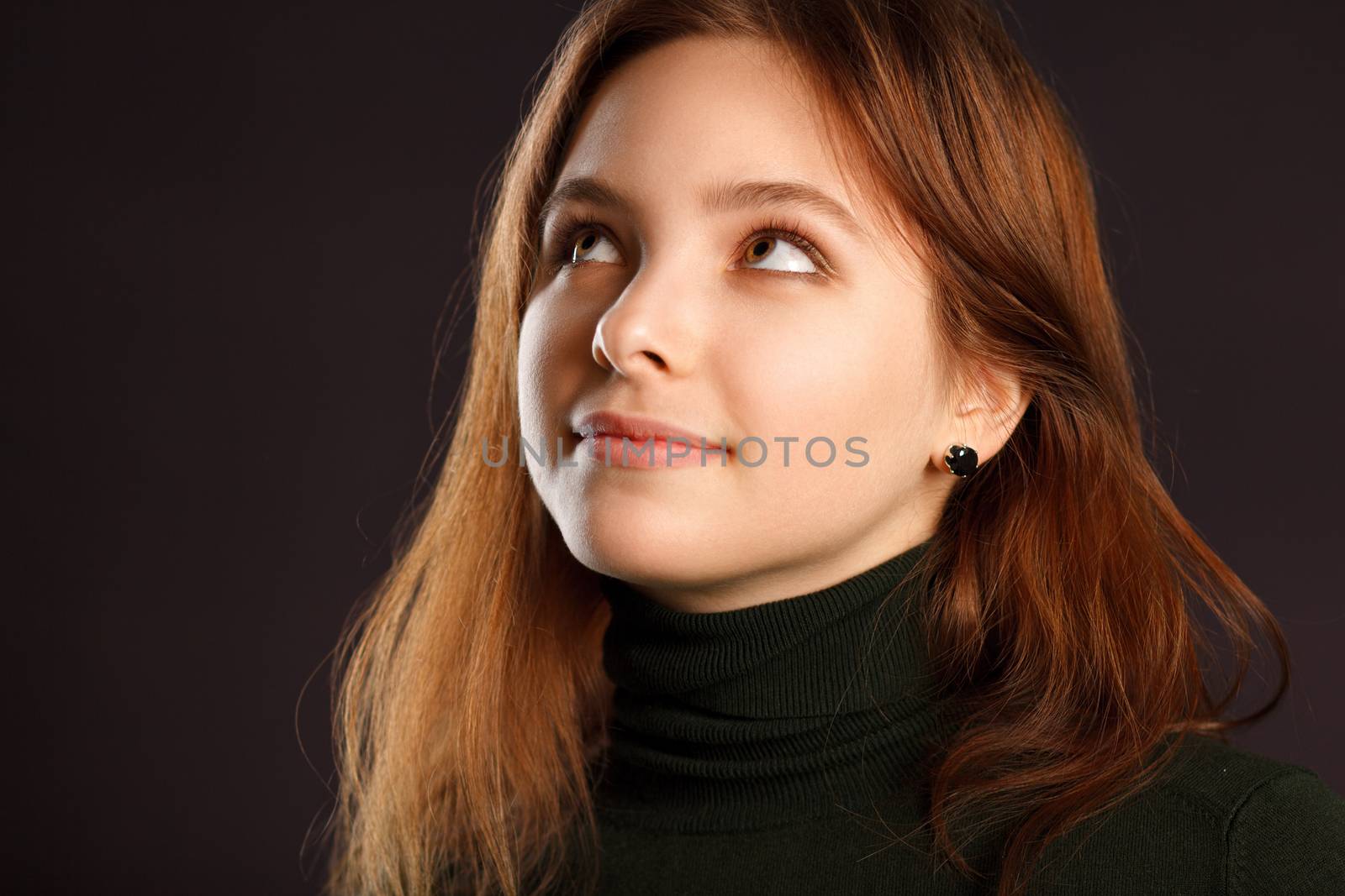 Closeup portrait of dreaming redhead woman looking up on dark background
