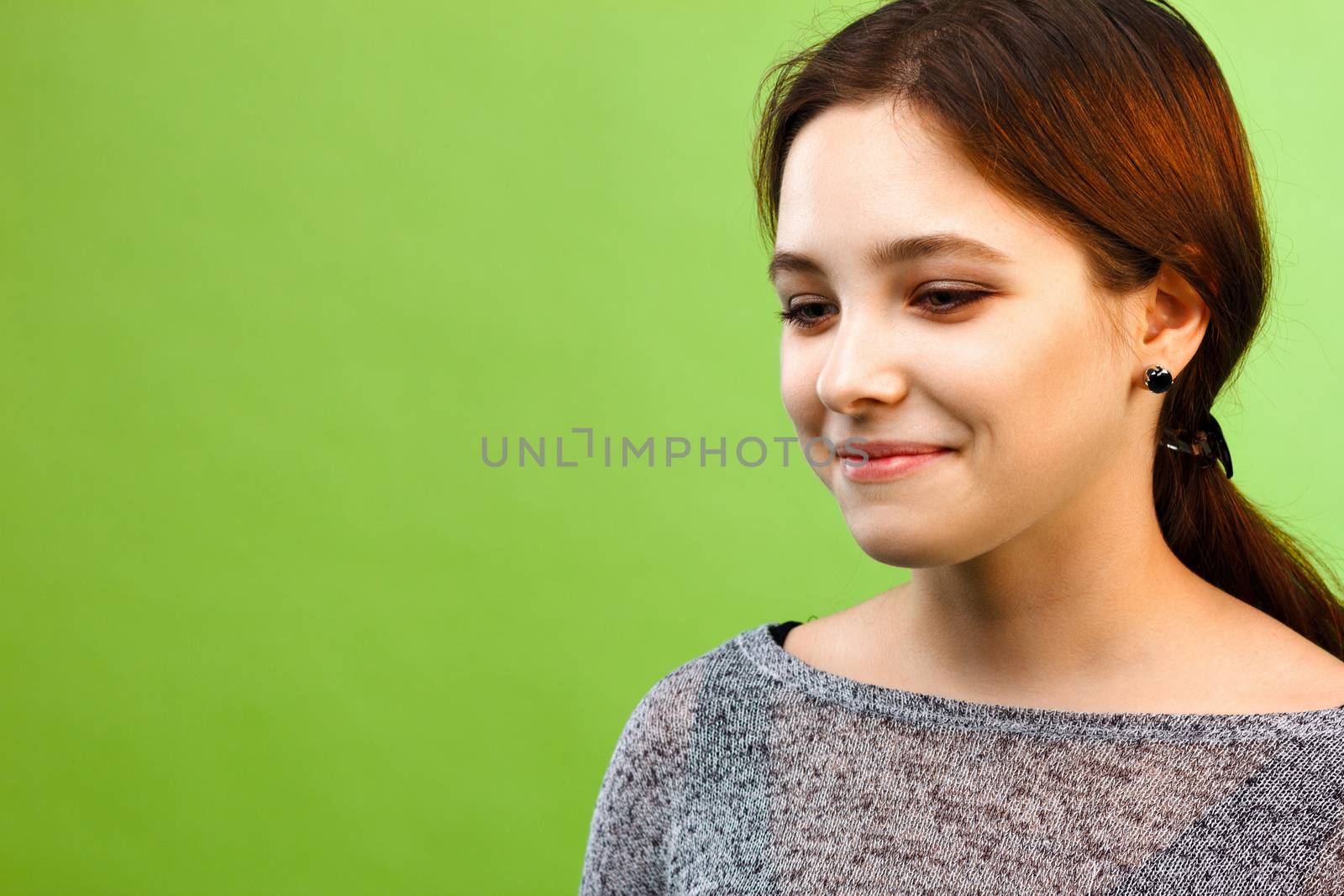 Portrait of cute smiling girl looking down on green background