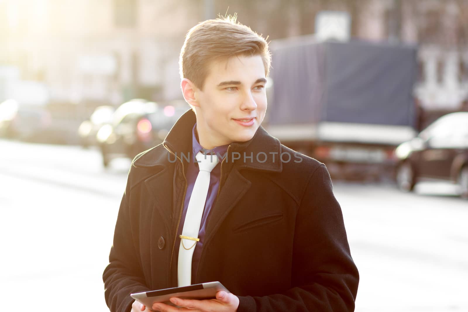 Young business man in black coat in street using tablet
