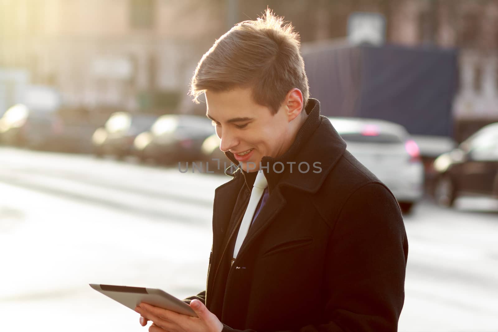 Young business man in black coat in street using tablet