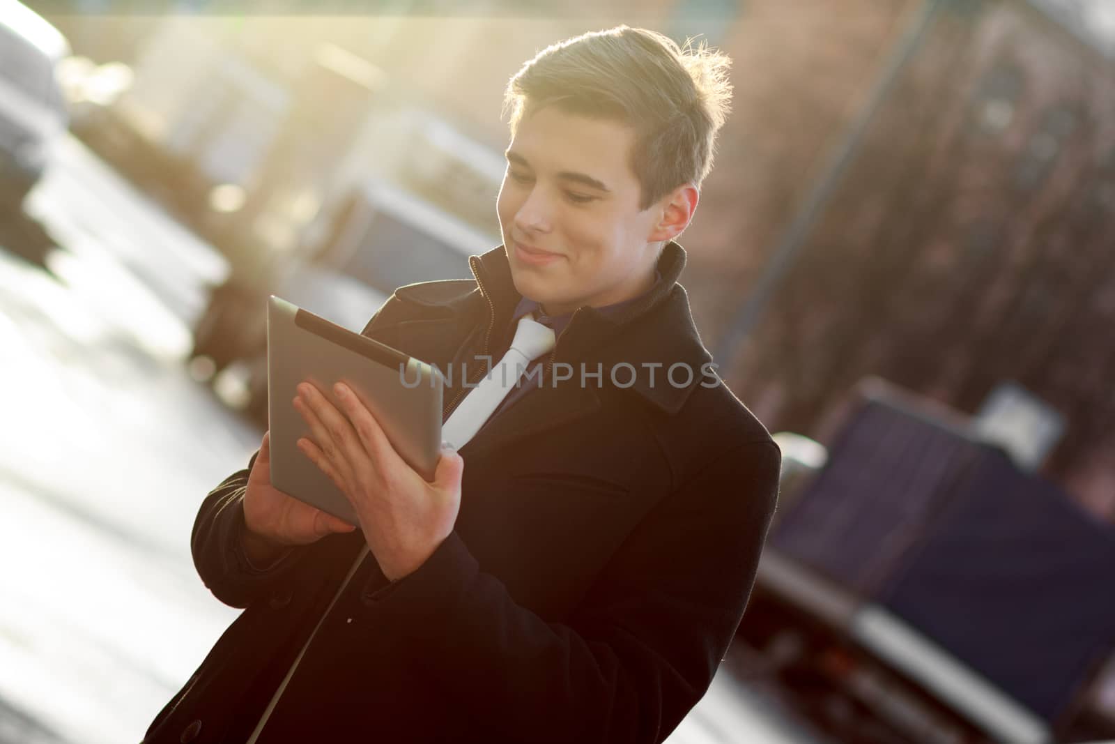 Young business man in black coat in street using tablet